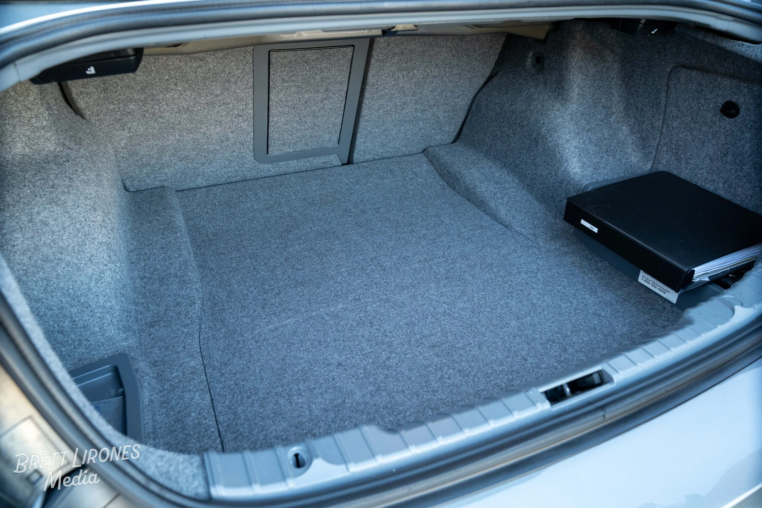 Empty car trunk with gray carpeting, a black box, and a small access panel.