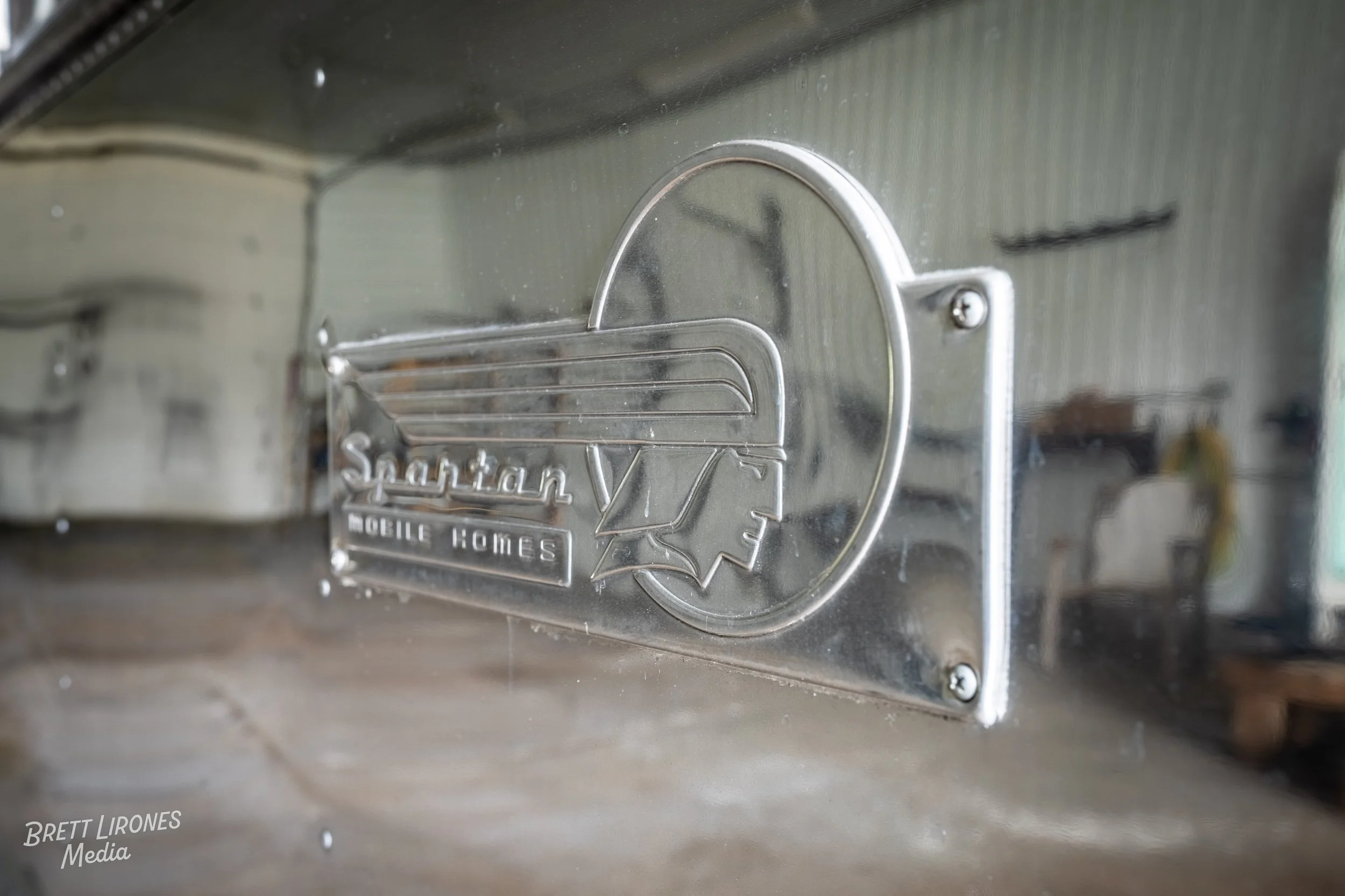 Close-up of a metal plaque with the logo and text 'Spartan V Mobile Homes' attached to a reflective surface.