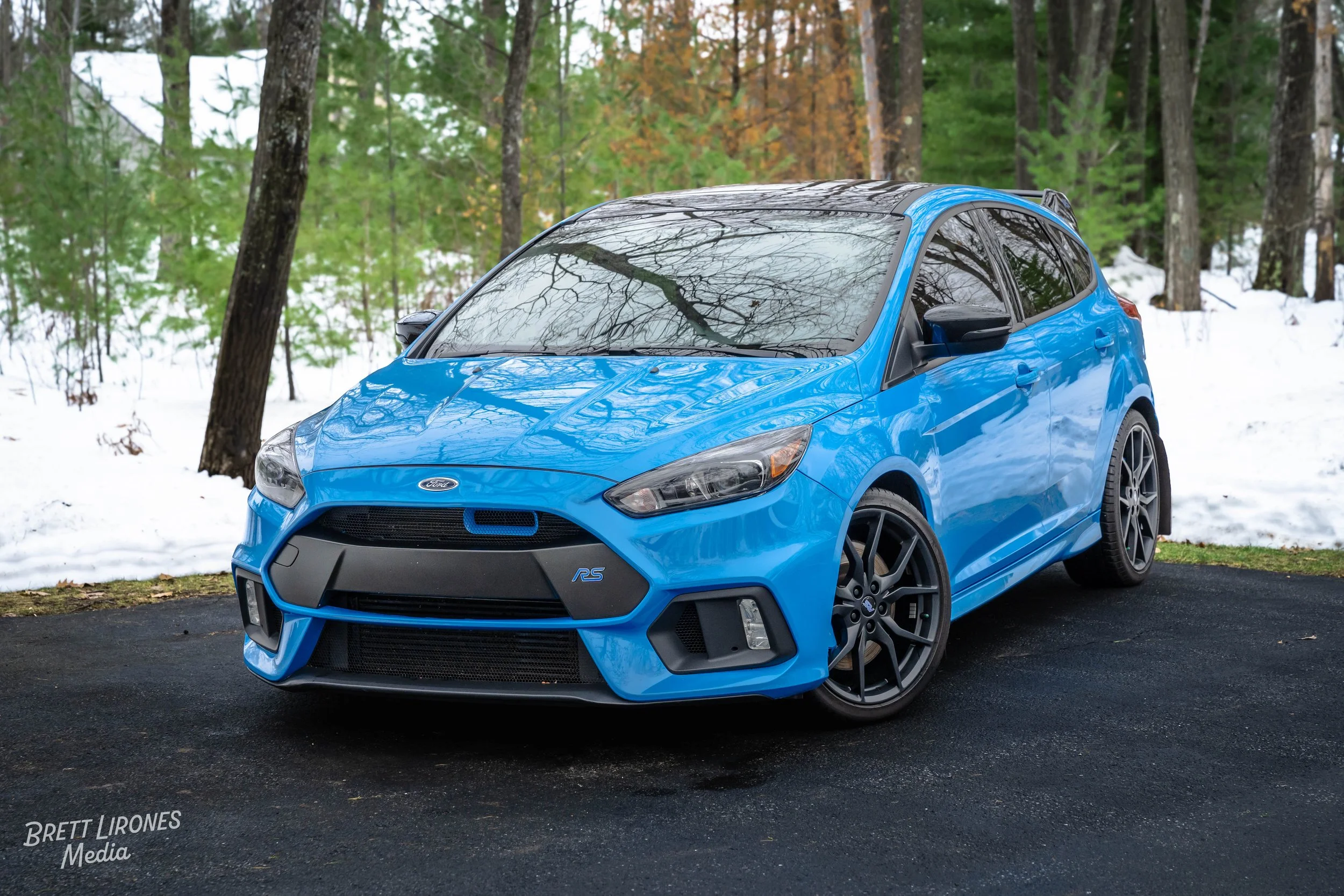 A blue Ford Focus RS parked on a paved surface in a snowy forested area.