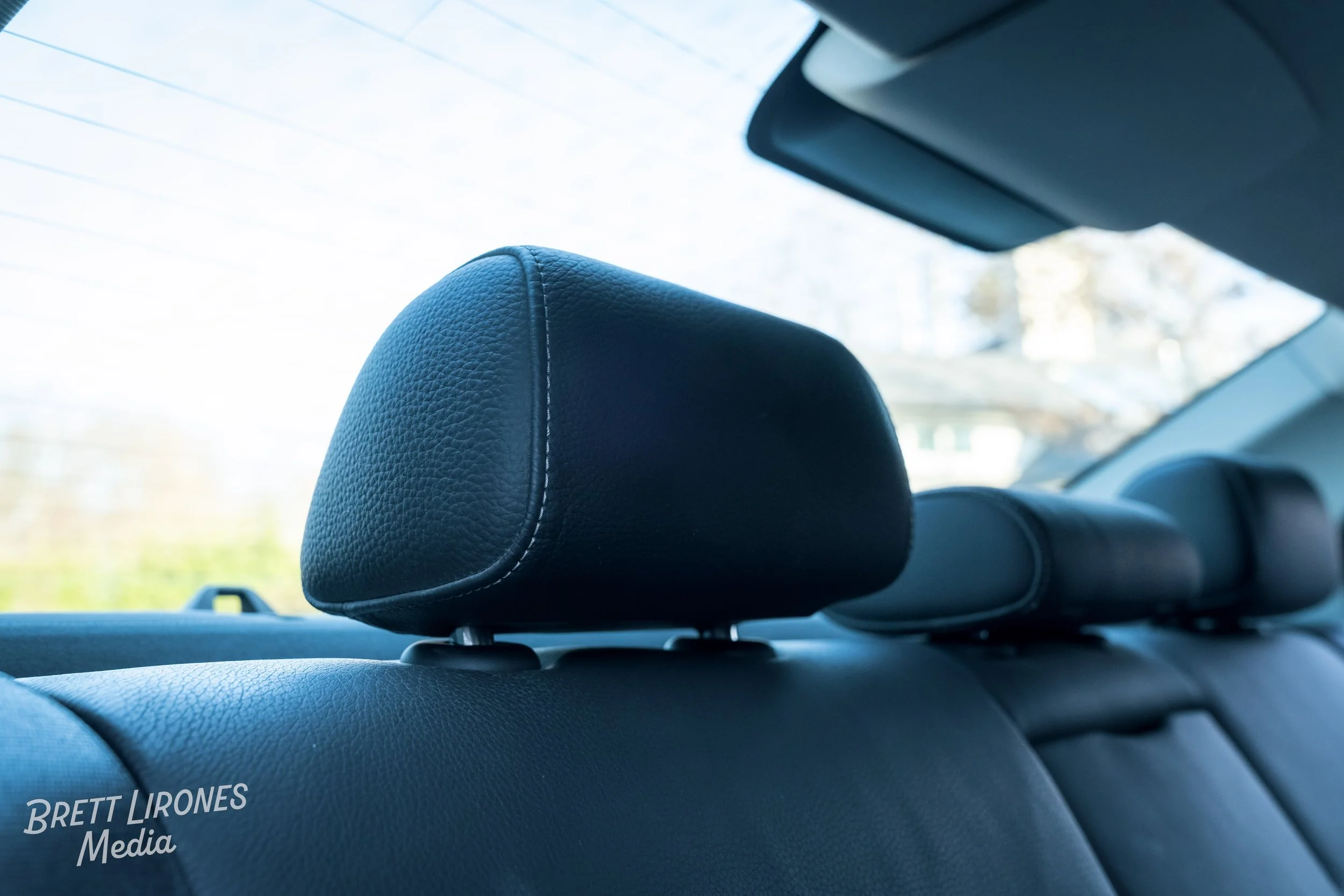 Close-up of a black leather headrest in a car interior with a clear view of a sunny outdoors through the back window.
