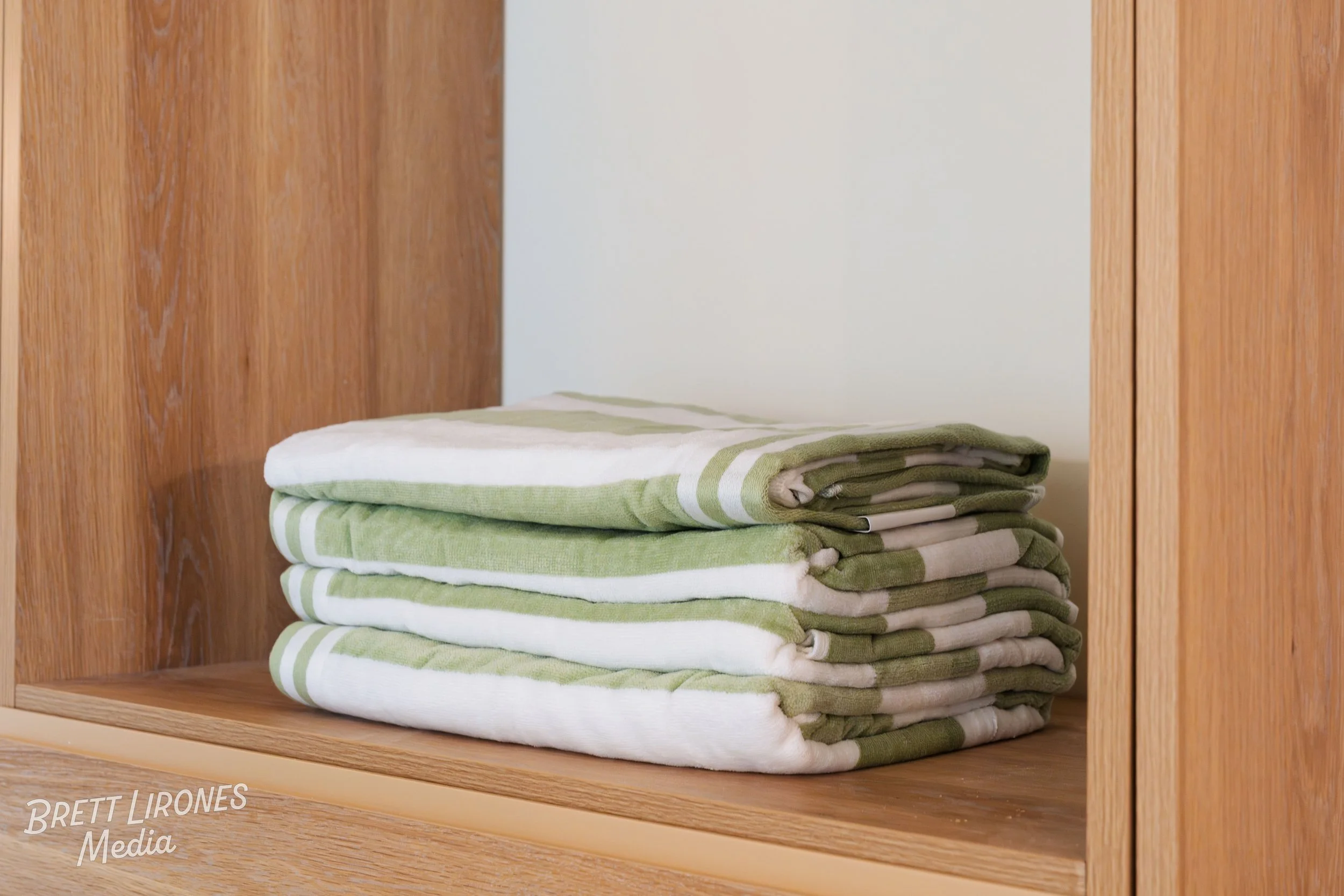 A neatly folded stack of green and white striped towels on a wooden shelf.