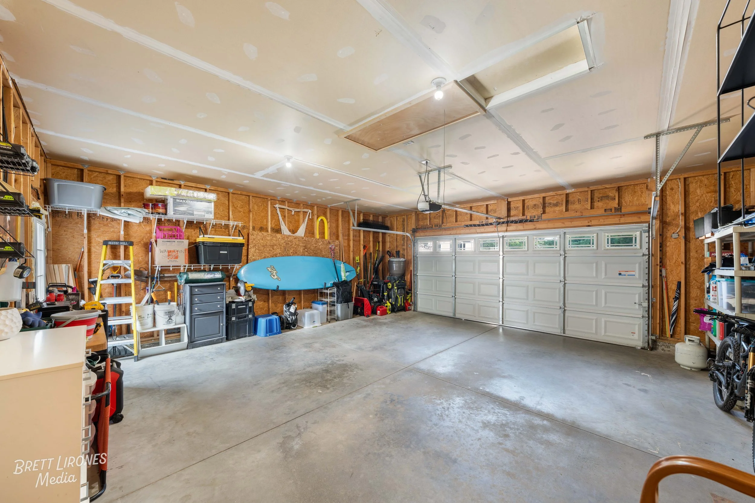 Empty garage with storage shelves, tools, and equipment along the walls, and a closed garage door at the back.