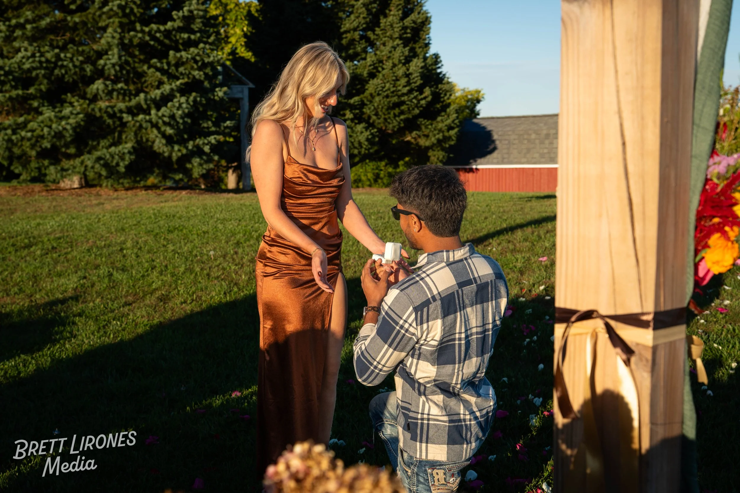 A man proposing to a woman during a garden proposal, with flowers and a wooden arch in the background.