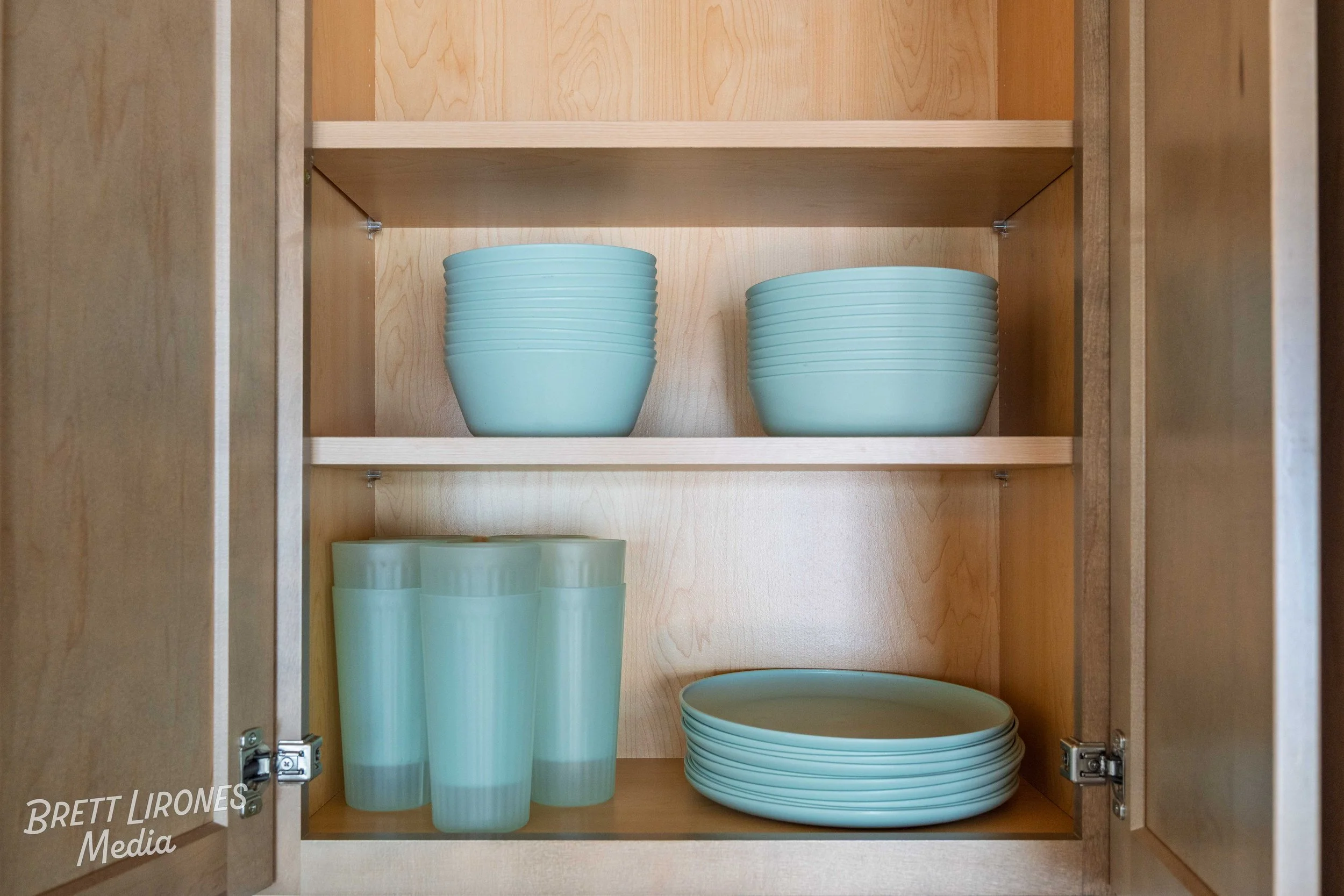 Open wooden cabinet with light blue bowls, plates, and glasses neatly arranged on shelves.