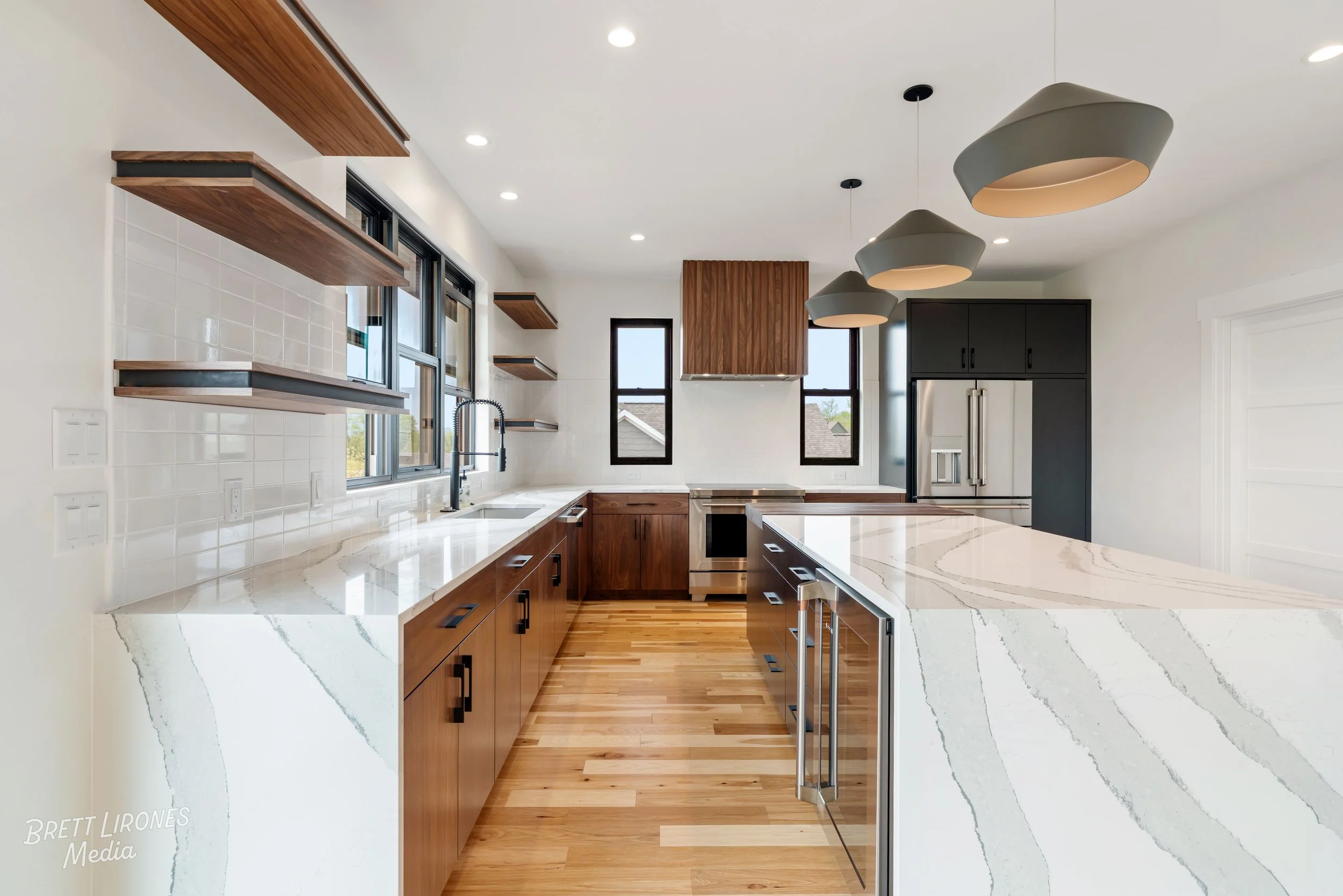 Modern kitchen with white countertops, wooden cabinets, black fixtures, stainless steel appliances, and pendant lighting.