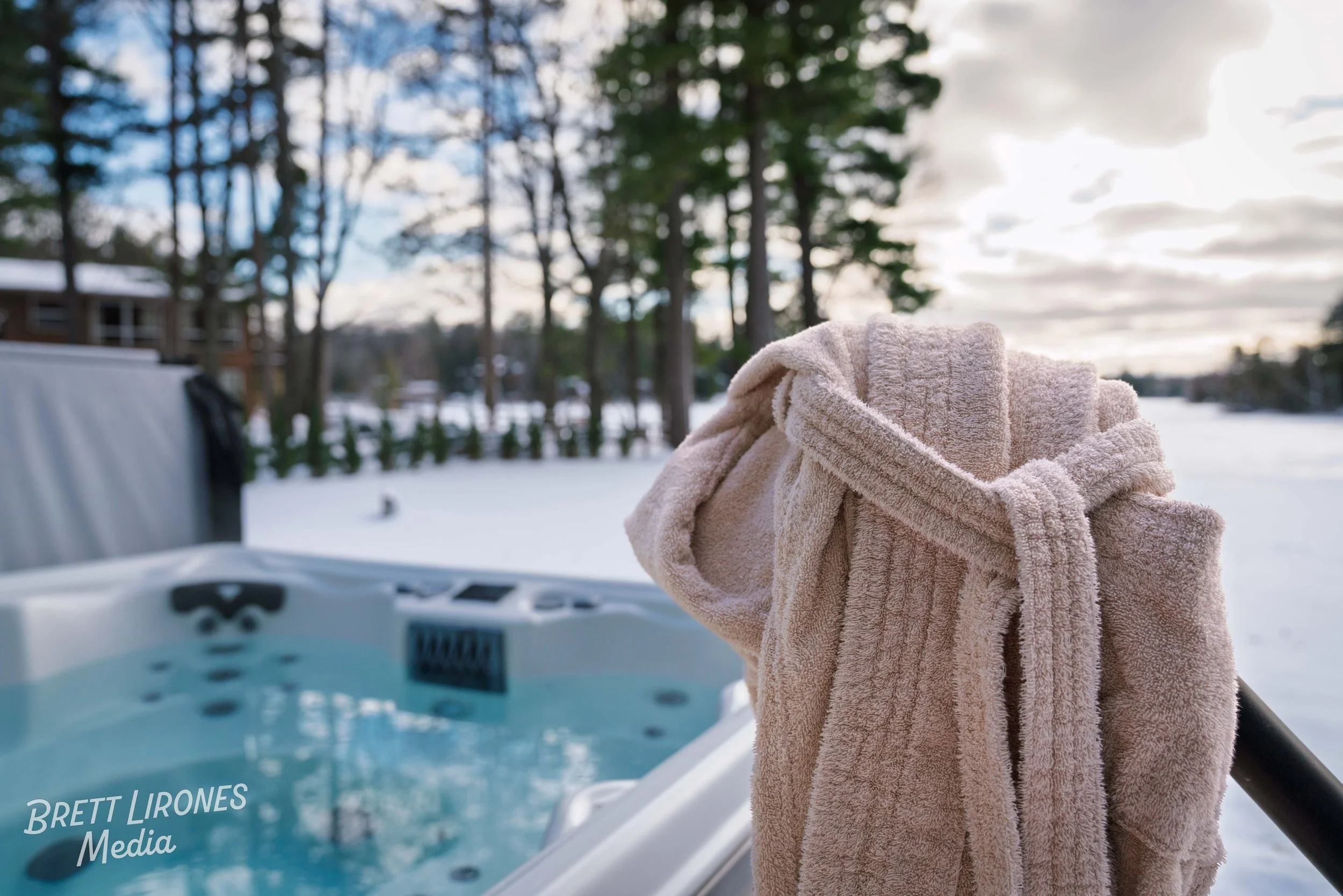 A beige towel hanging on a railing with a hot tub and snow-covered landscape in the background, trees, and a partly cloudy sky.
