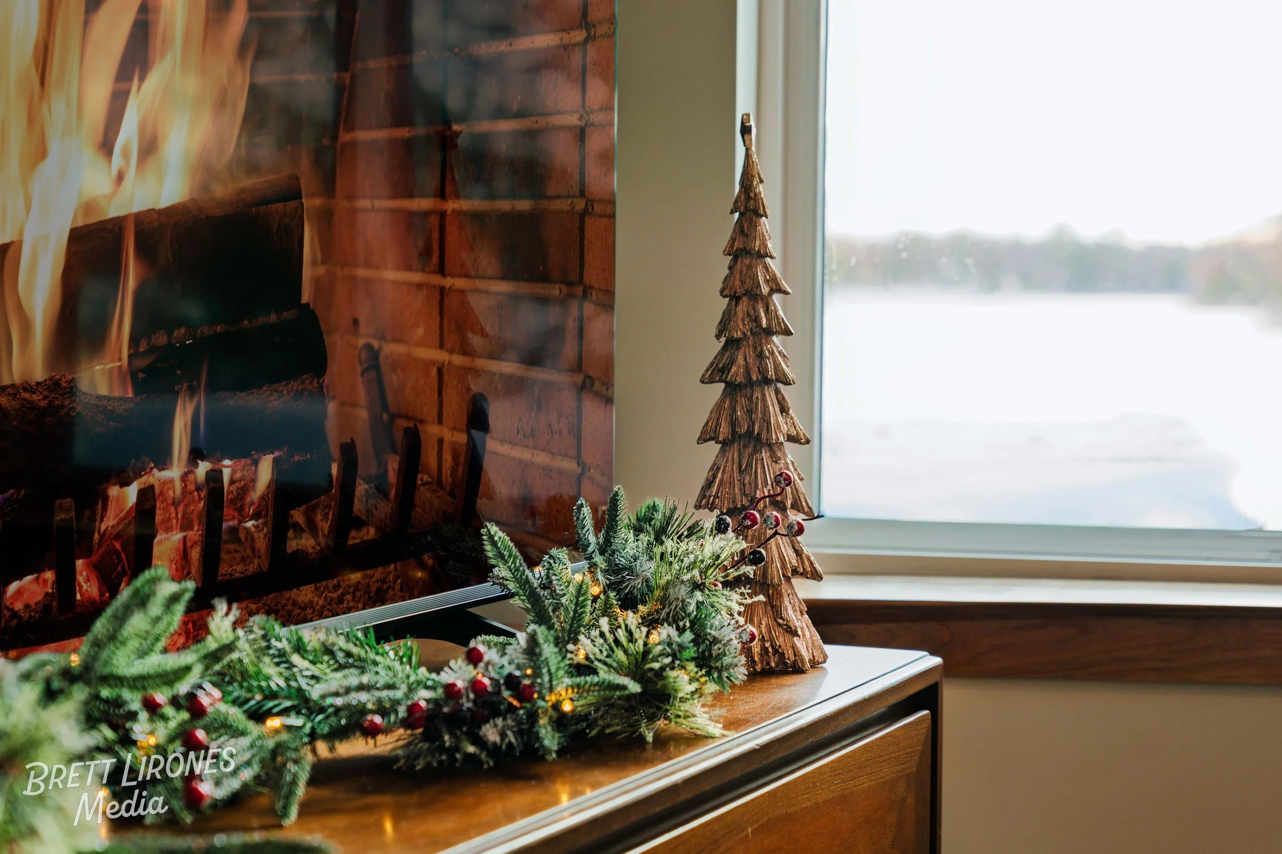 Decorative Christmas arrangements on a wooden surface near a window, including faux greenery, red berries, and a wooden Christmas tree