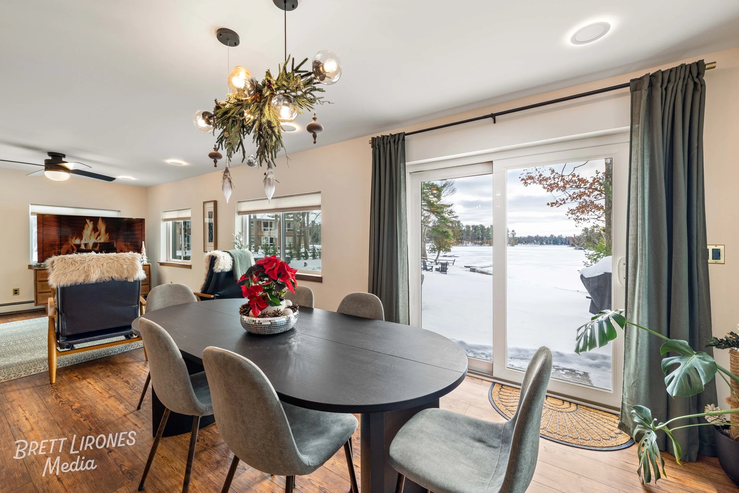 Dining room with window view of snow-covered outdoor scene, indoor holiday decorations, and a dark wood dining table with gray chairs.