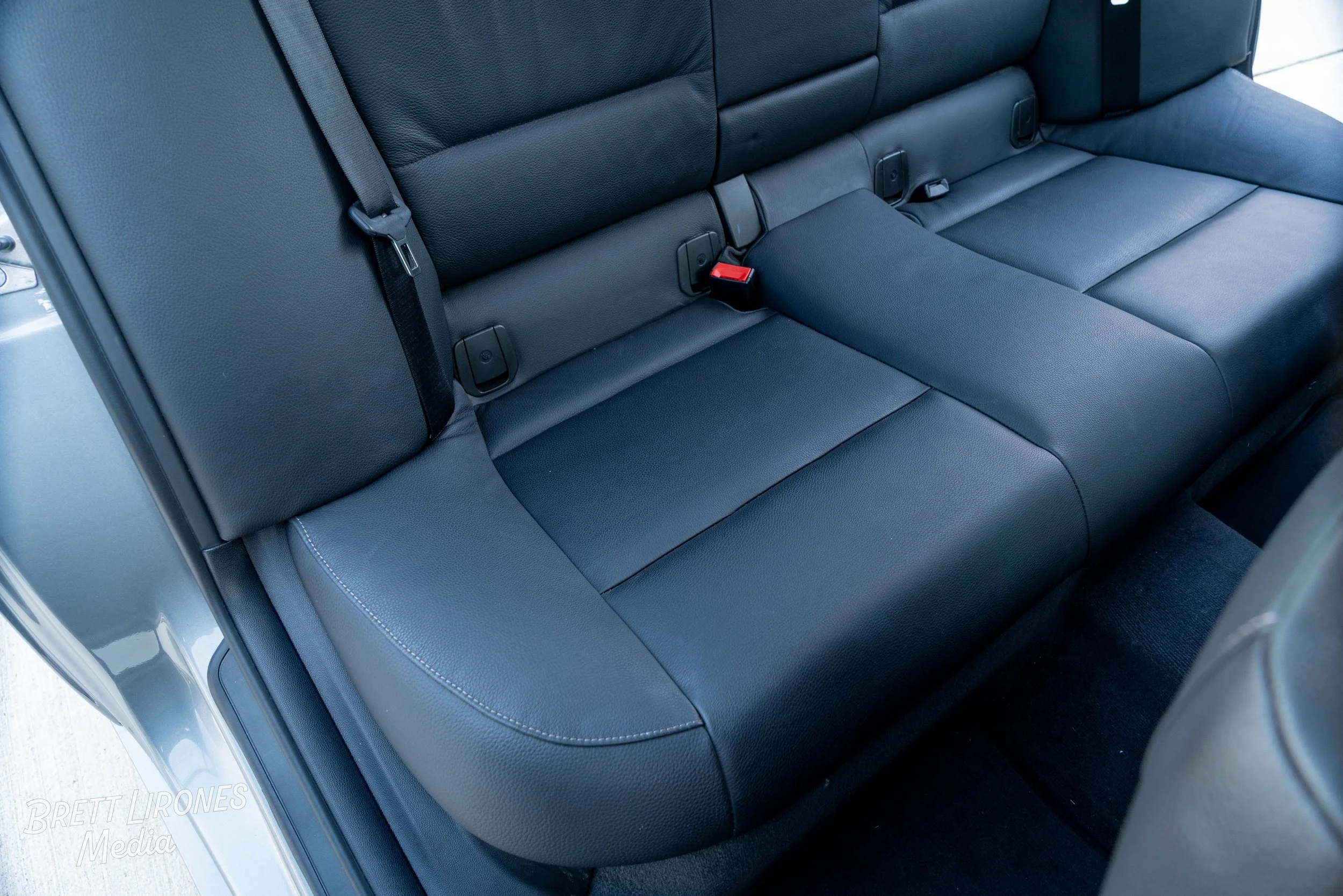 Black leather back seat of a vehicle with seatbelt buckles and stitching details.