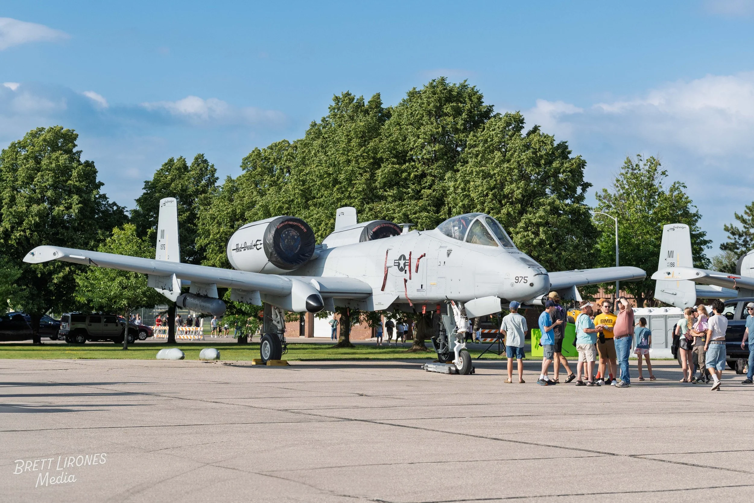 A group of people touring a military aircraft, an A-10 Thunderbolt II, displayed outdoors on a sunny day with trees in the background.