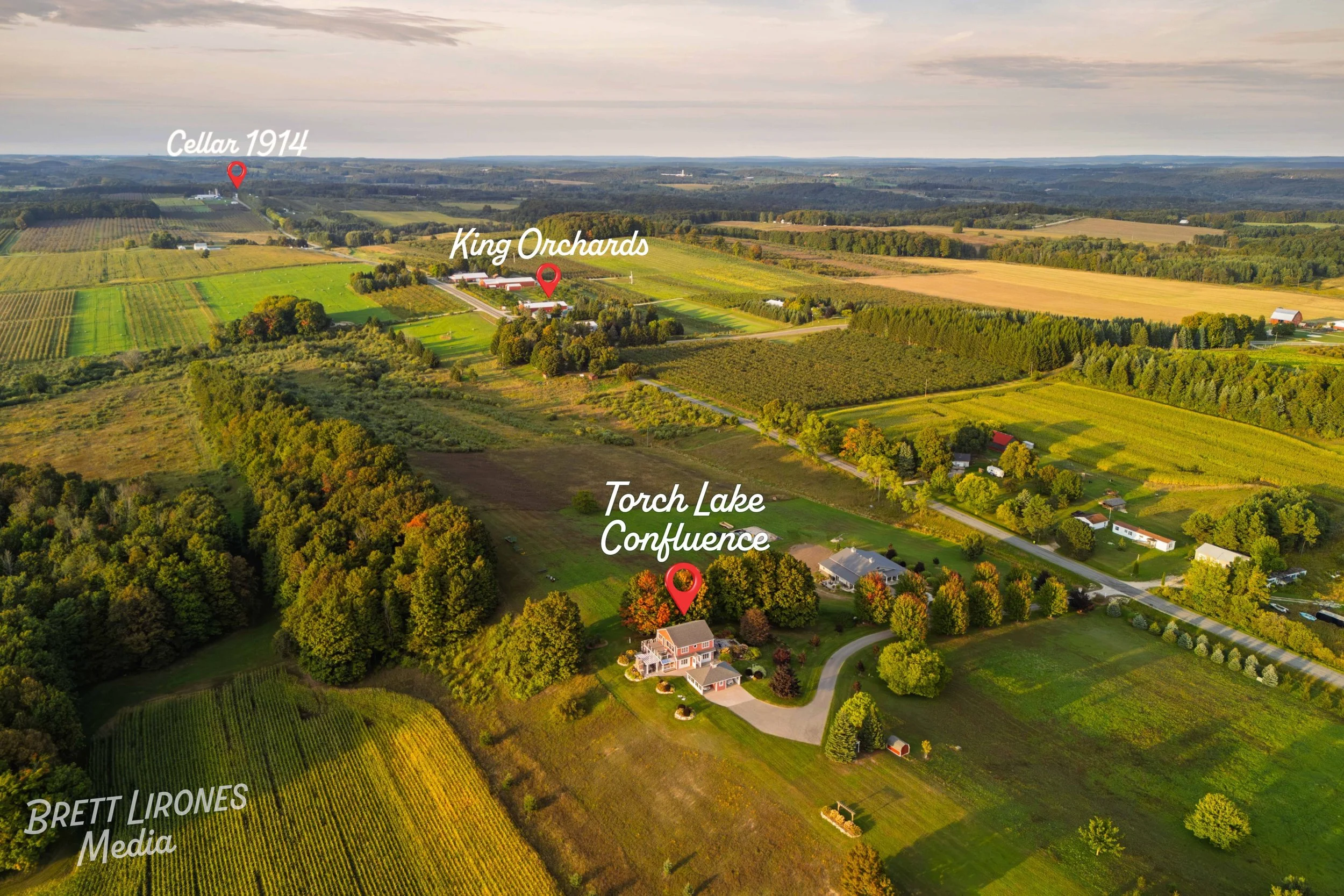 Aerial view of a rural landscape with farms, fields, and trees. The image highlights the Torch Lake Confluence and King Orchards, with labels and location markers. The sunset light illuminates the countryside.