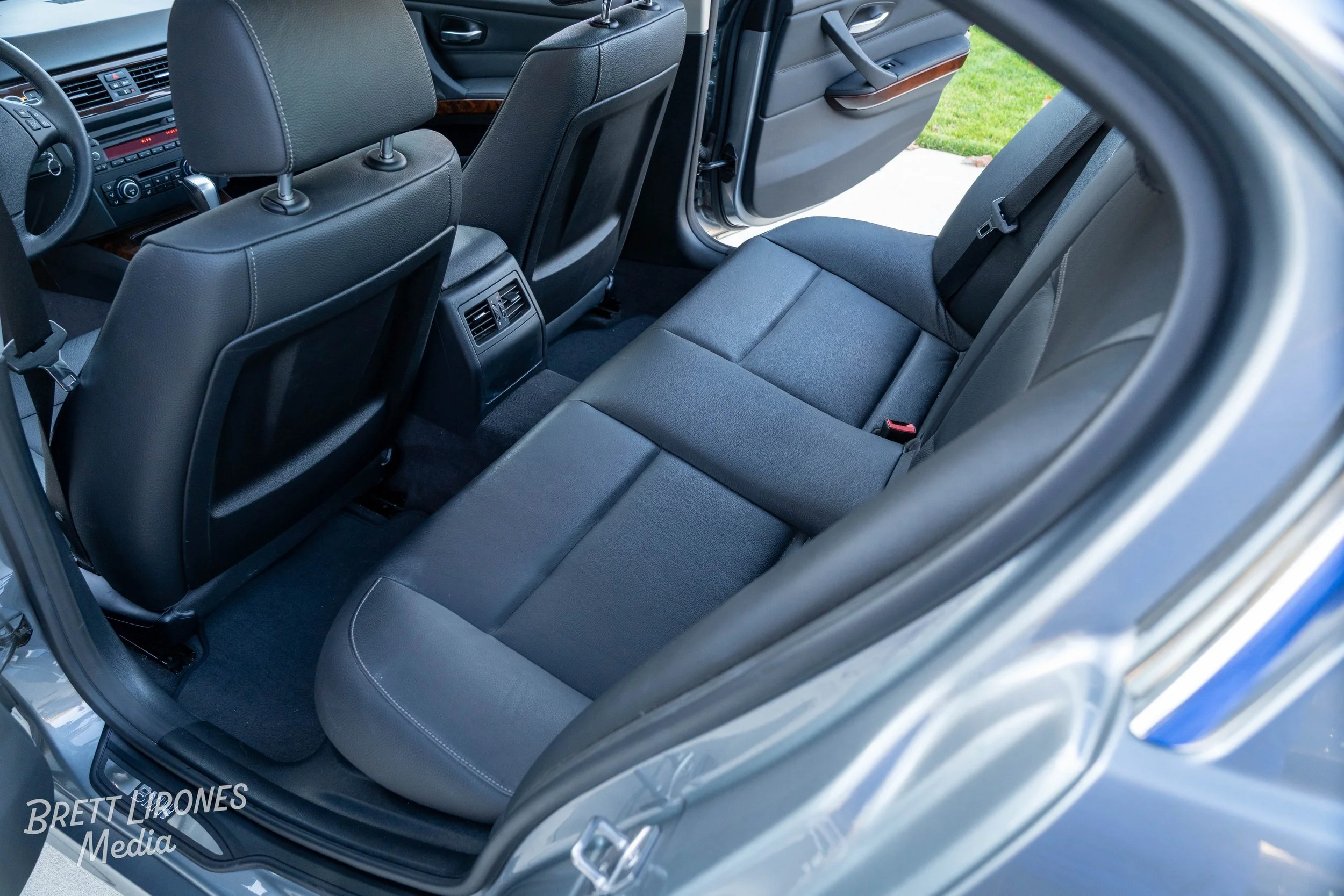 Inside view of a car's back seat area, showing black leather upholstery, rear seats, front seats, and the open rear car door.