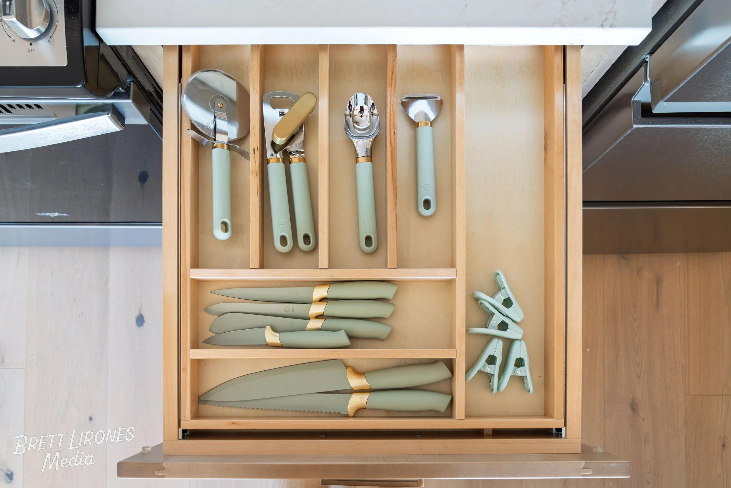 Kitchen drawer containing a set of green-handled knives, a set of green-handled kitchen utensils including a ladle, slotted spoon, and serving spoon, and several green-handled cloth clips.