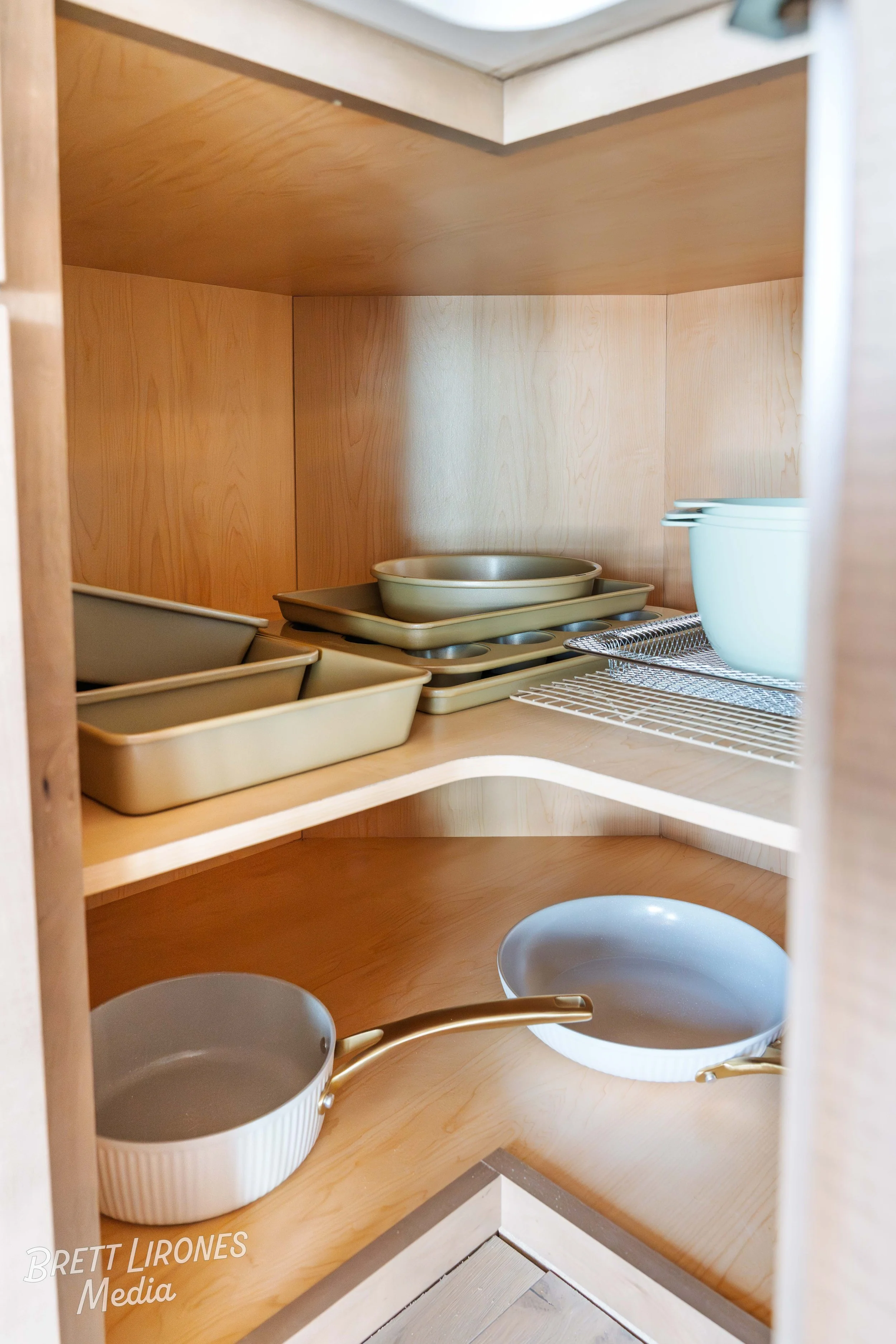 Open wooden kitchen cabinet with beige baking trays, metal cooling racks, and blue mixing bowls inside.