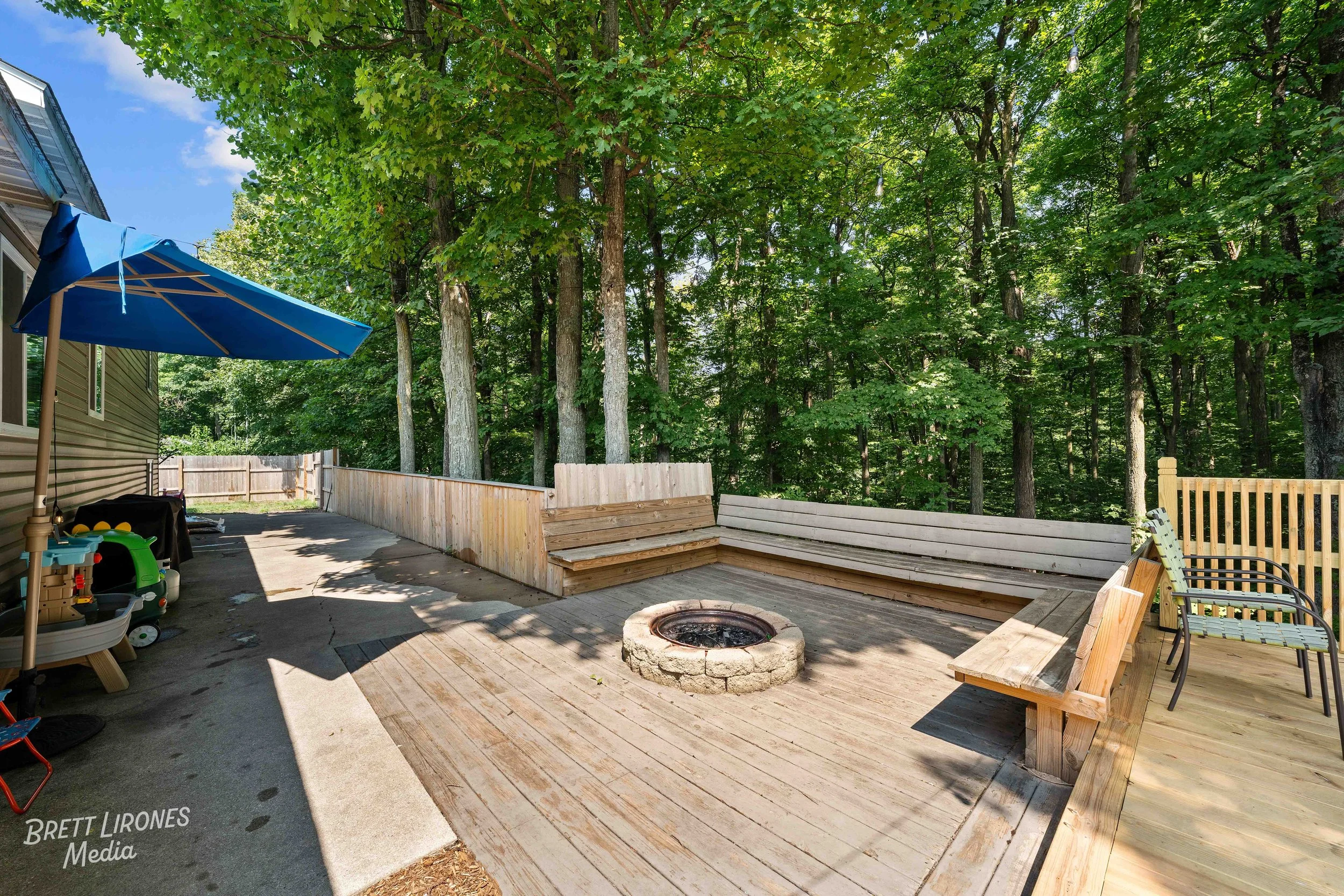 Backyard patio with seating area, fire pit, blue umbrella, and surrounding trees