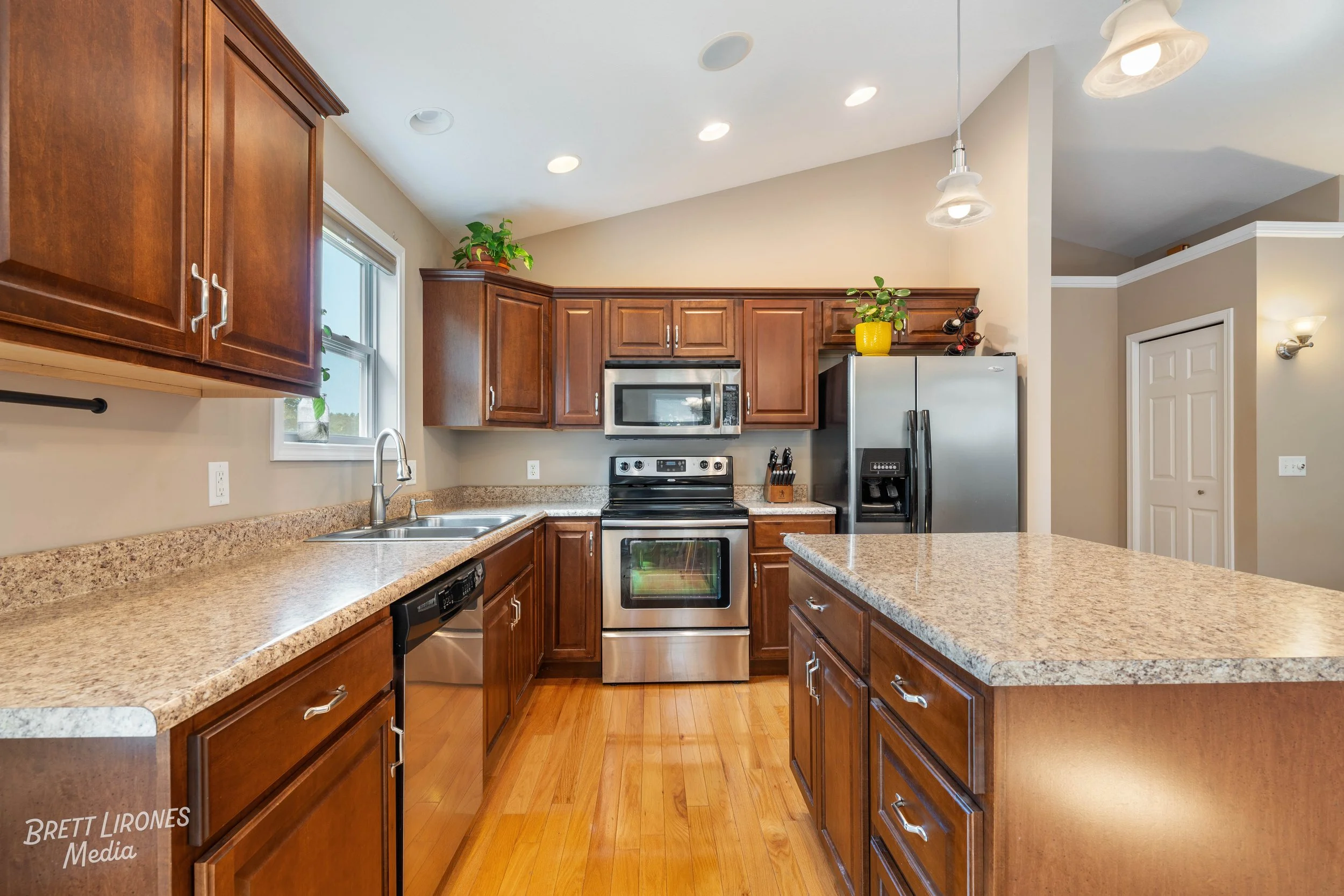 Kitchen with wooden cabinets, granite countertops, stainless steel appliances, and hardwood flooring.