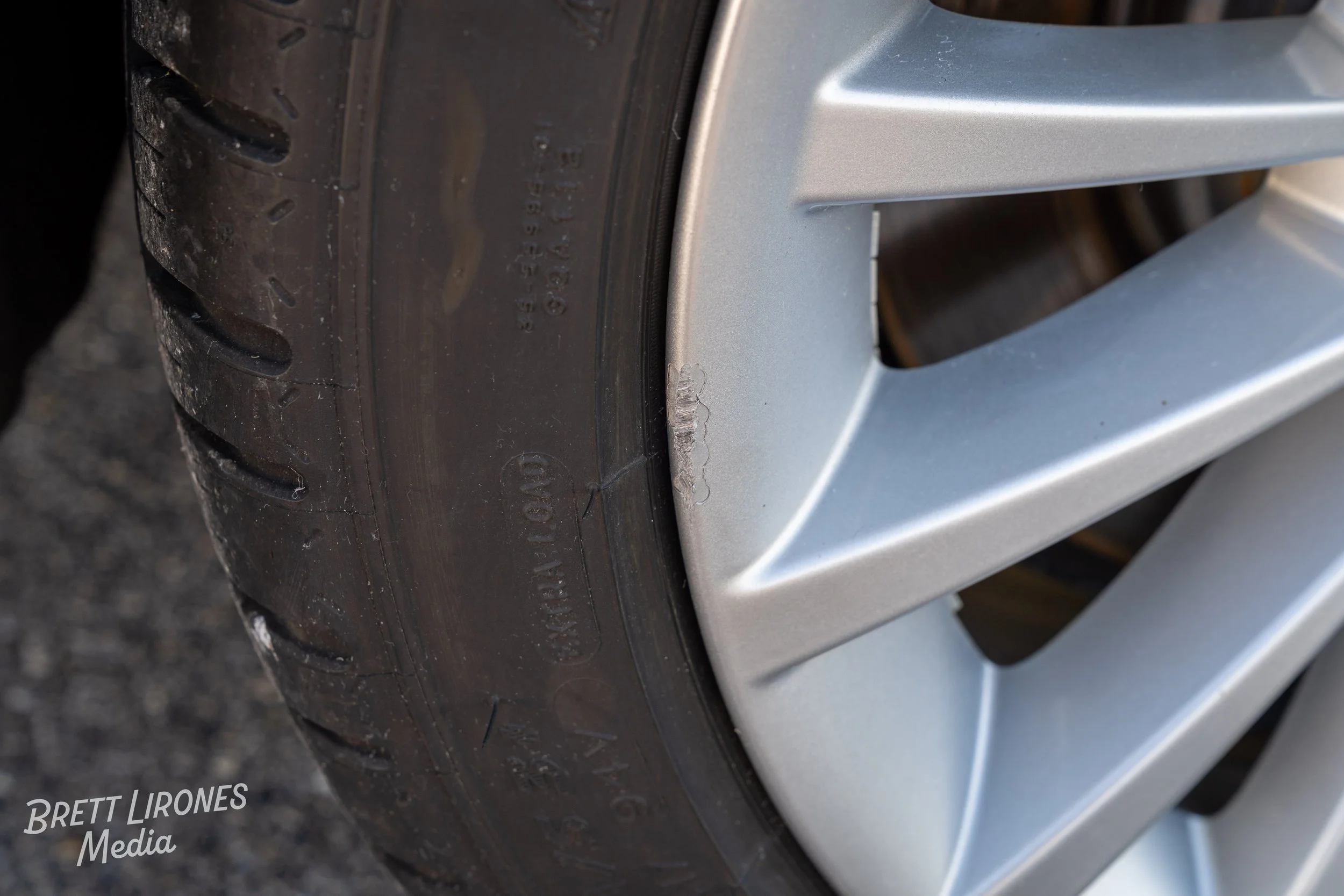 Close-up of a car wheel with a curb rash on the silver alloy rim, and a black tire with visible tread.