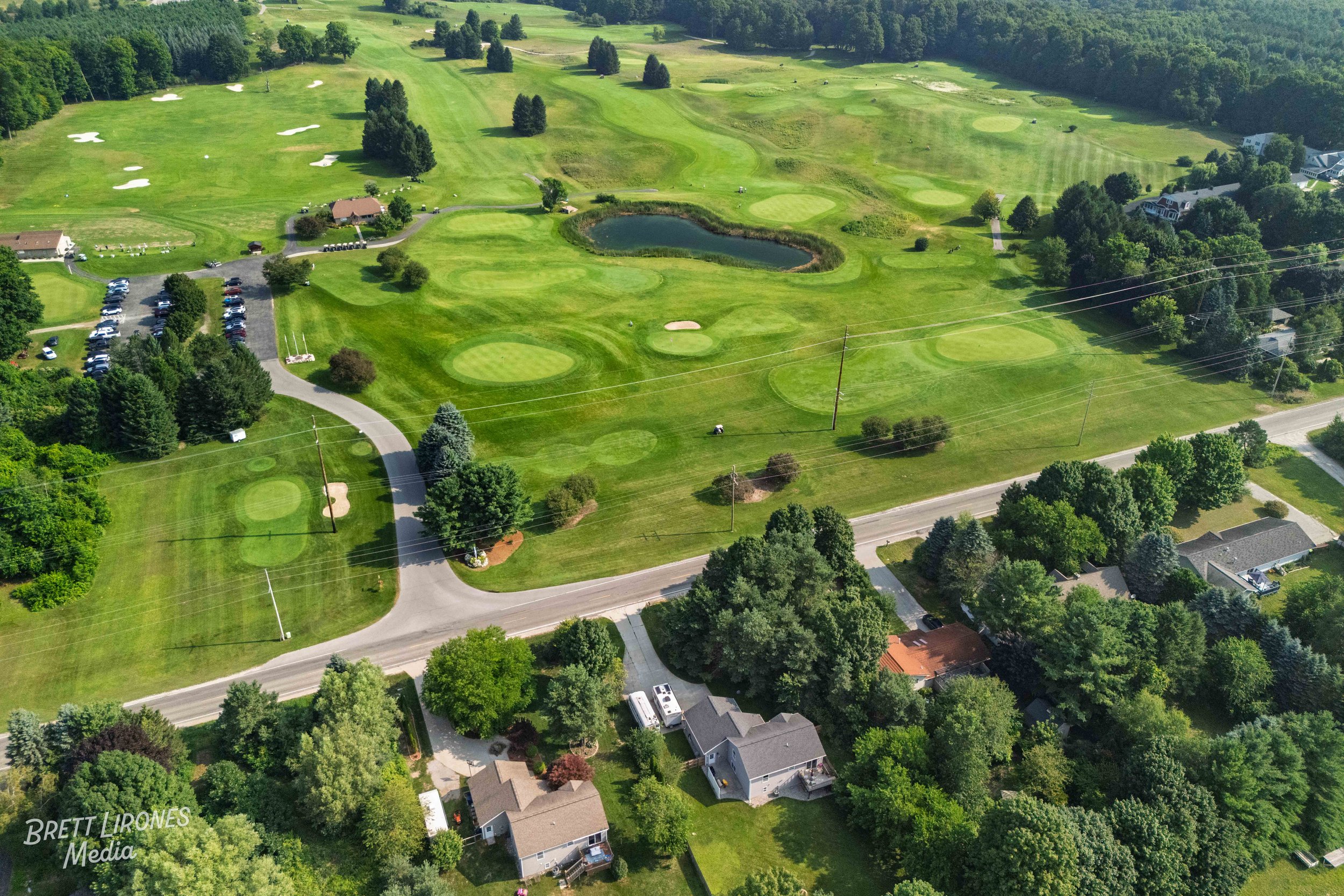 Aerial view of a golf course with sand traps, water hazards, greens, fairways, and surrounding homes and trees.