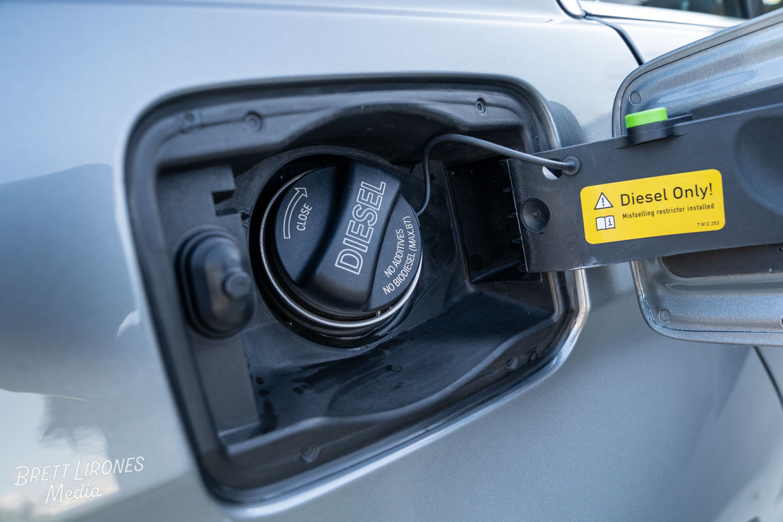 Close-up of a car's fuel filler cap labeled 'DIESEL' inside the fuel door, with a yellow sticker indicating 'Diesel Only! Misfueling restrictor installed'.