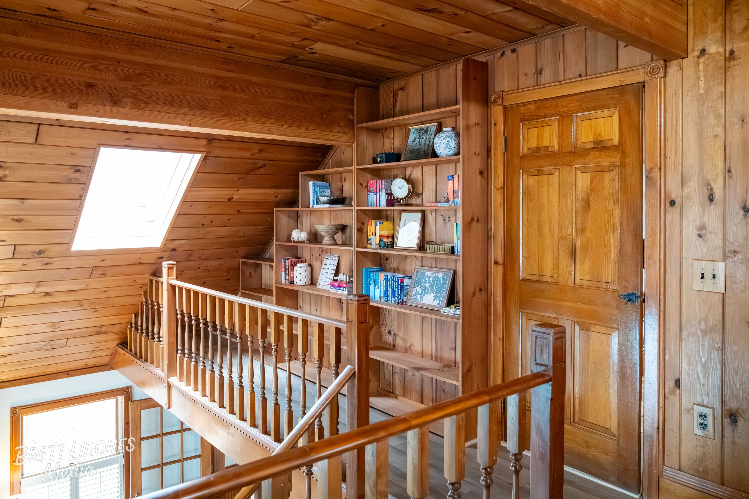 Wooden interior with bookshelf, skylight window, and staircase railing.