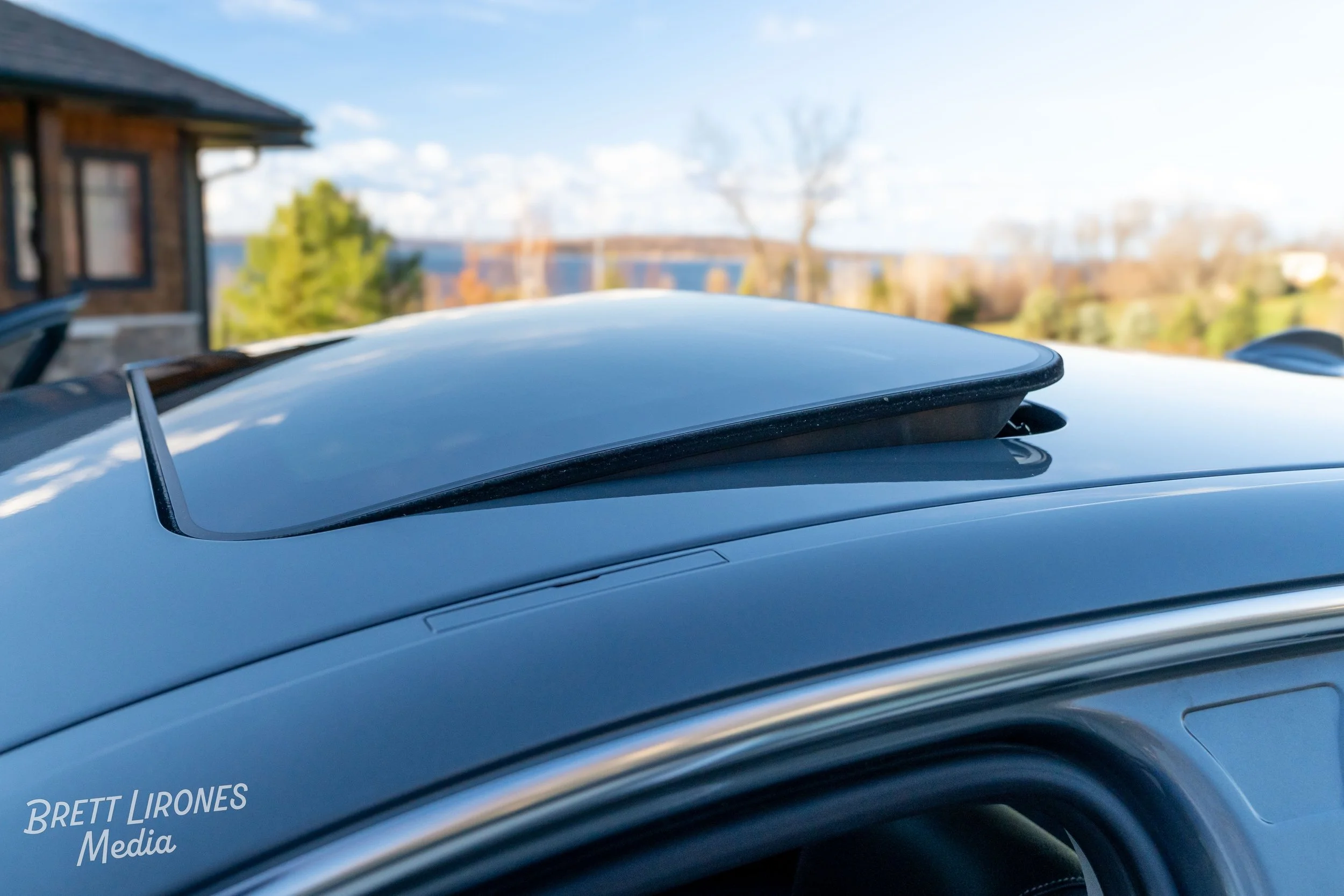 Close-up of a car's raised sunroof with a clear blue sky and houses in the background.