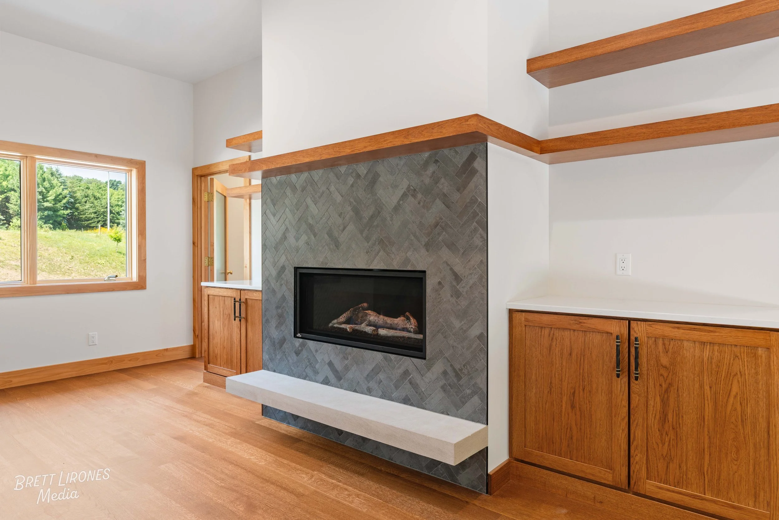 Living room with a modern fireplace, wooden shelves, cabinets, and a window showing greenery outside.