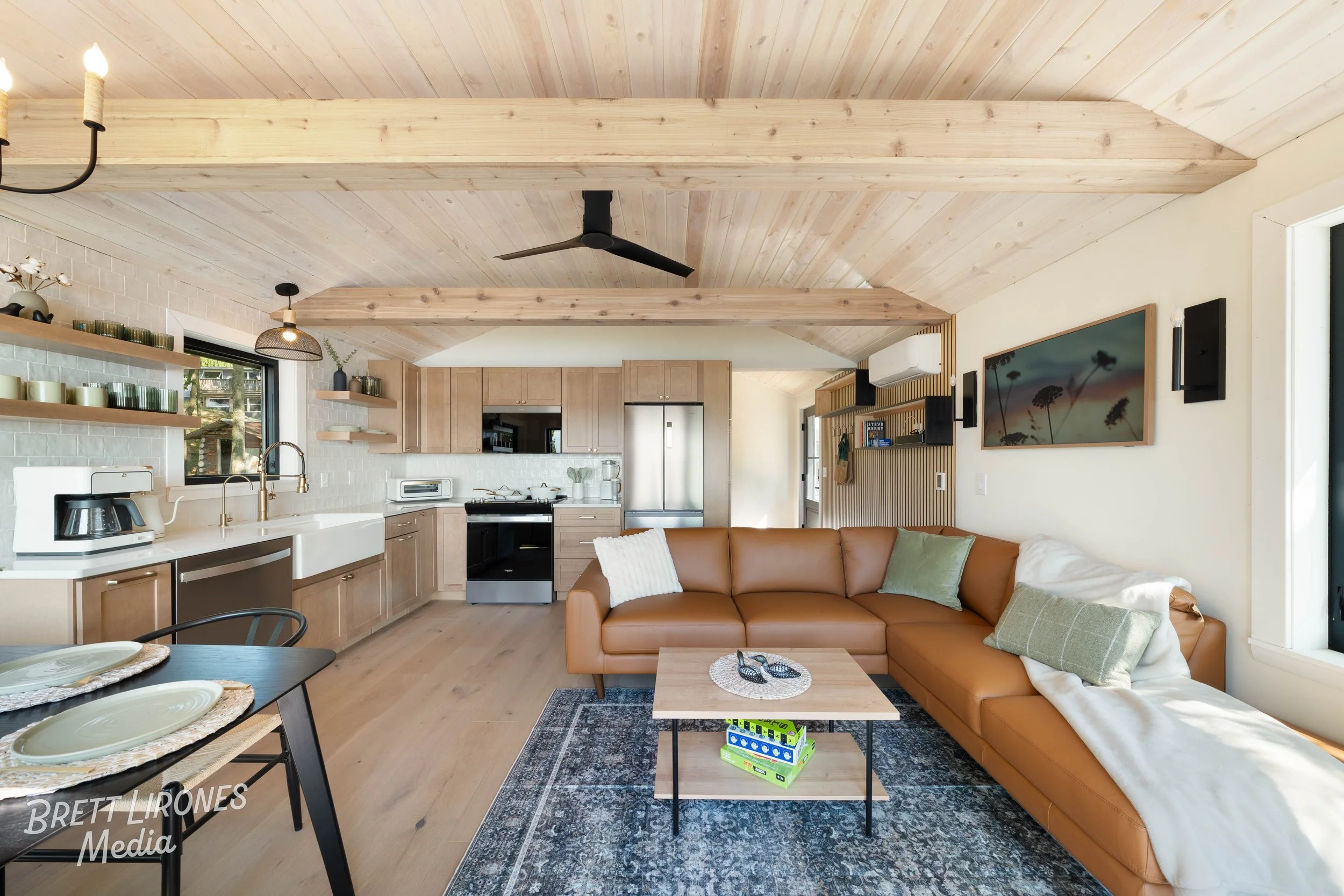 Open-concept living room and kitchen with wood accents, a leather sofa, a coffee table, and kitchen cabinets.