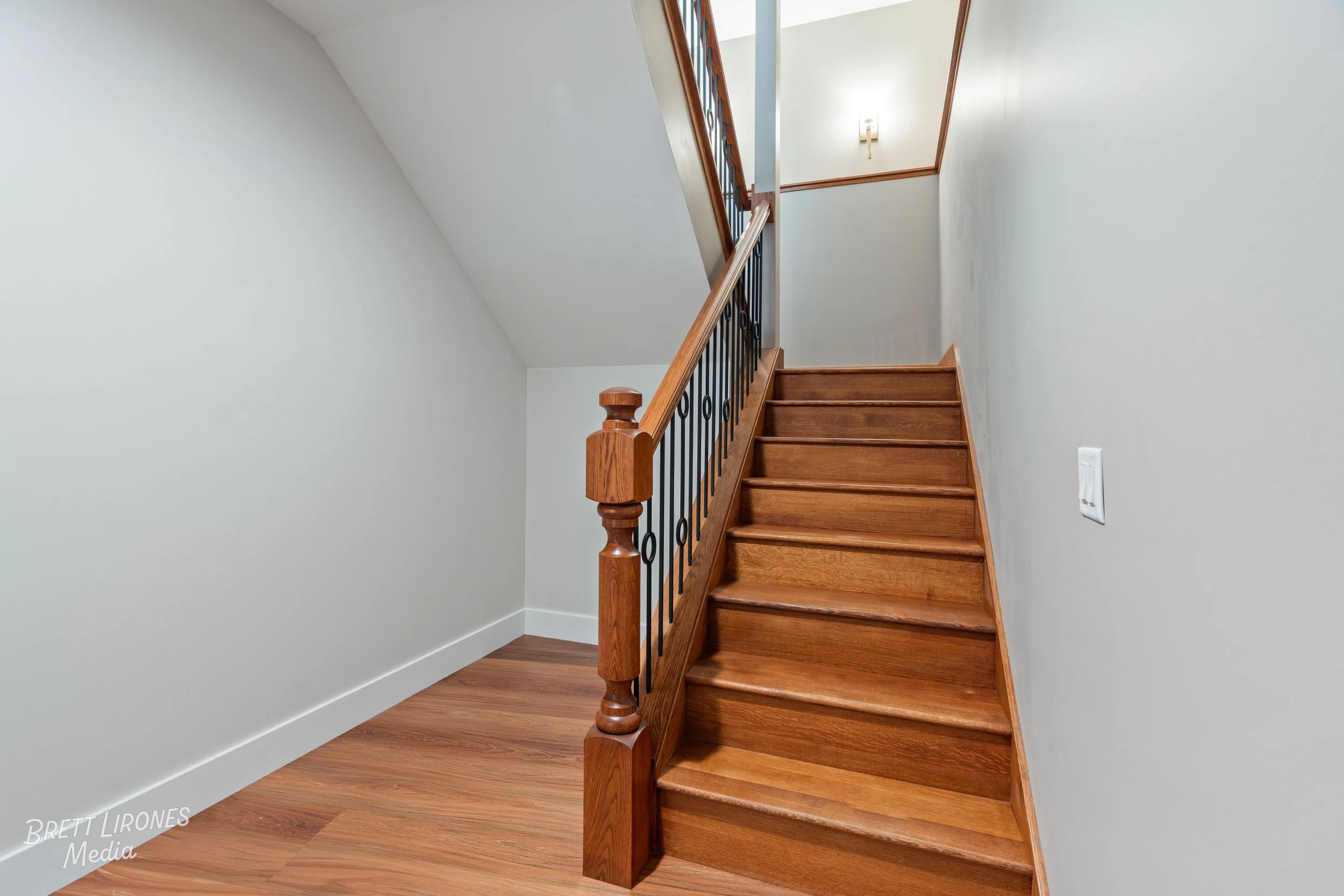 Wood staircase with black metal railing in a residential interior, with white walls and a wooden floor at the base.