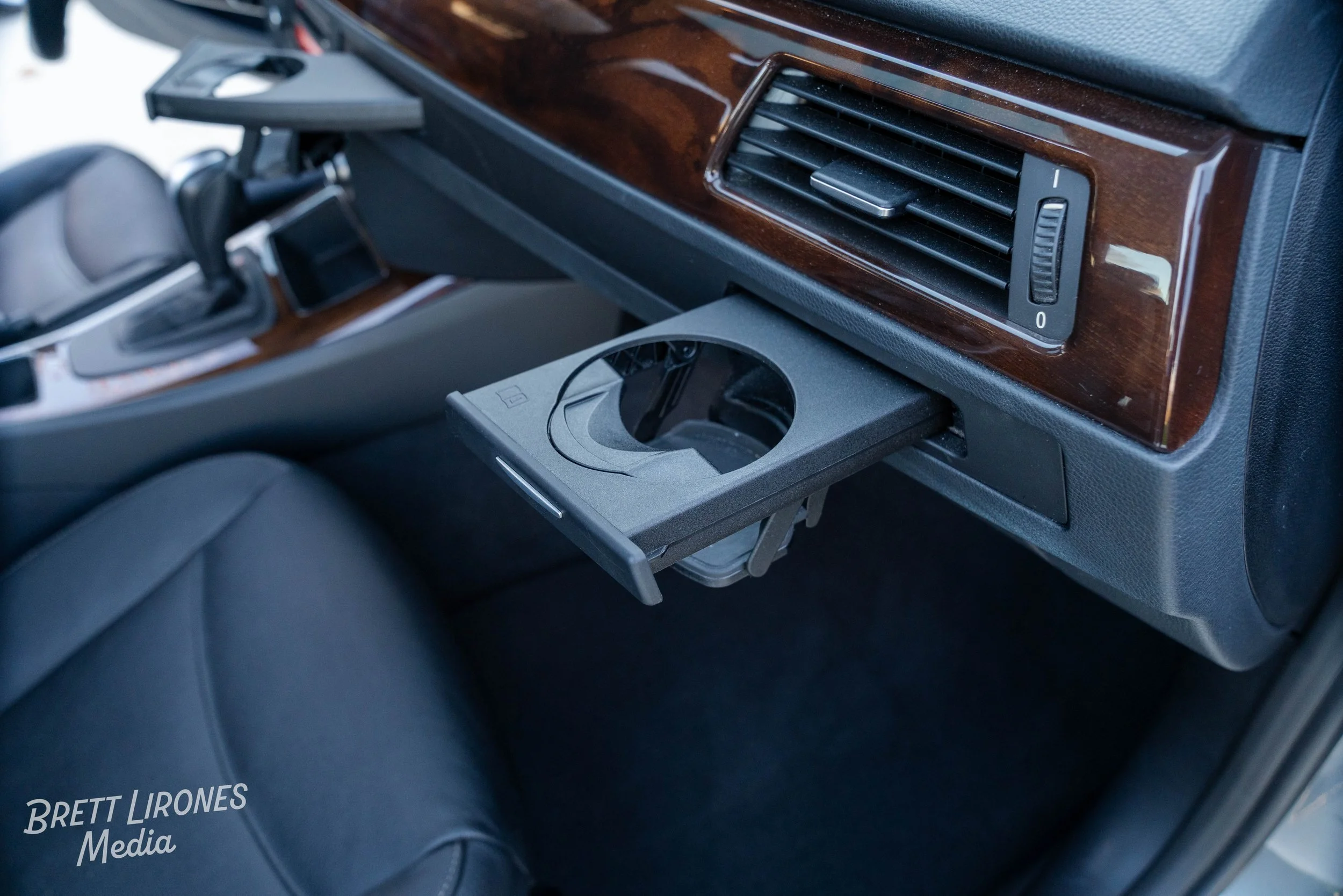 Inside a car, showing a fold-out cup holder and an air vent with a control slider on a wooden trim dashboard.
