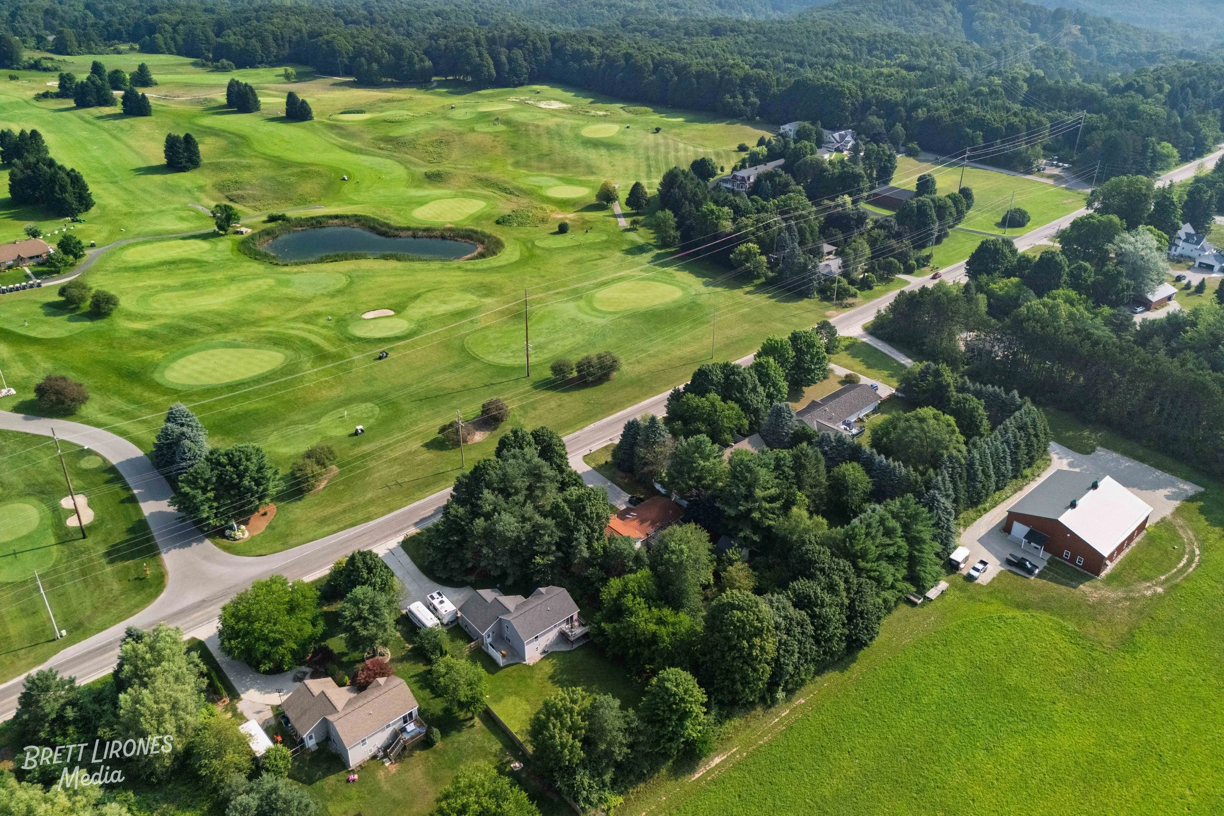 Aerial view of a golf course with multiple greens, water hazards, and trees surrounded by residential houses and lush green areas.