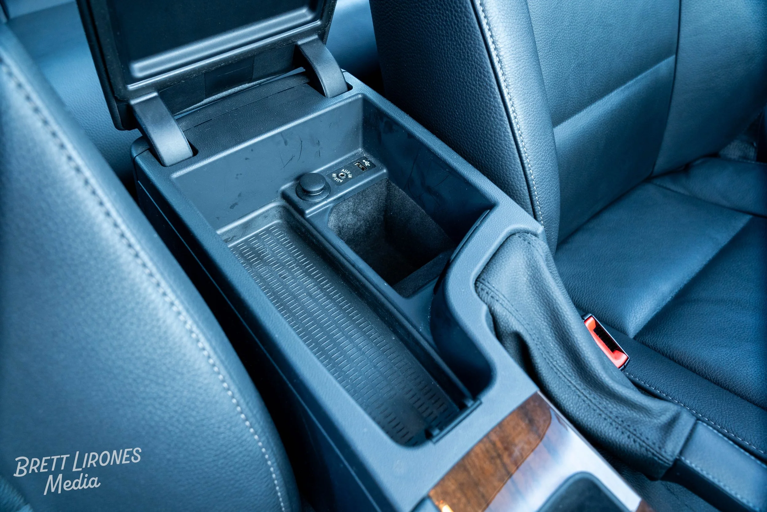 Interior of a car showing the center console with an empty storage compartment, a switch, and the handbrake next to leather seats.