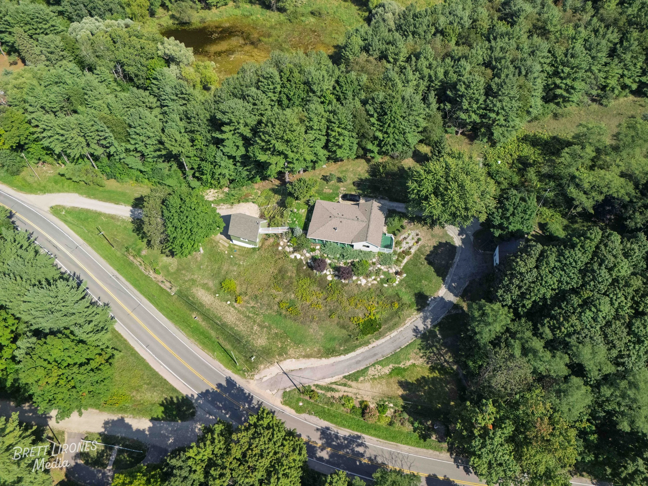 An aerial view of a house surrounded by trees with a driveway and a road nearby.