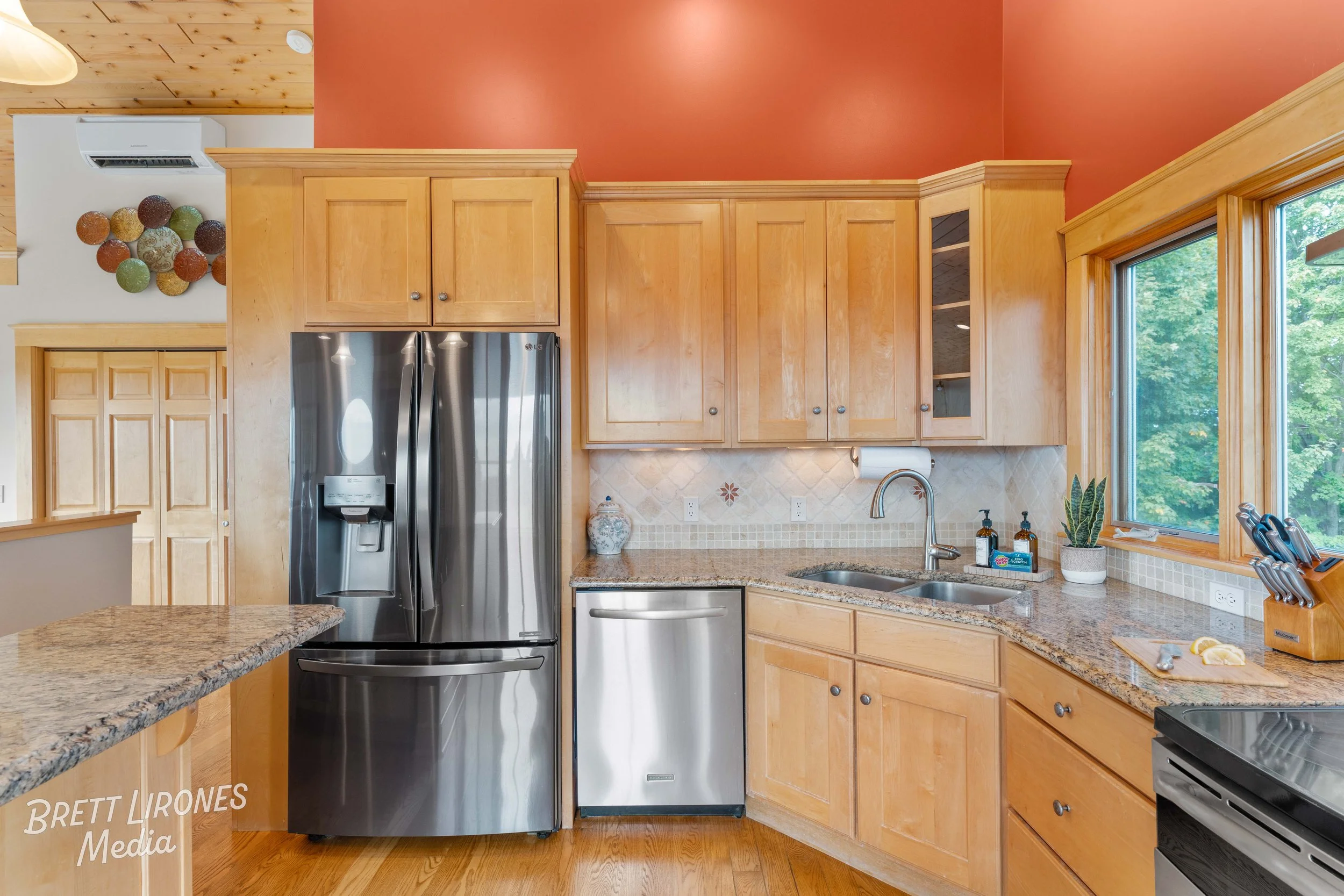 Kitchen with wood cabinets, granite countertops, stainless steel refrigerator, small dishwasher, a sink, and a window overlooking green trees.