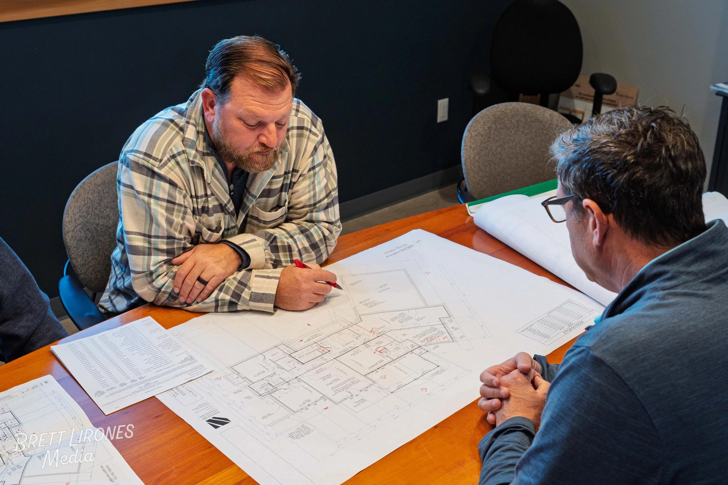 Two men reviewing architectural blueprints at a conference table in an office.