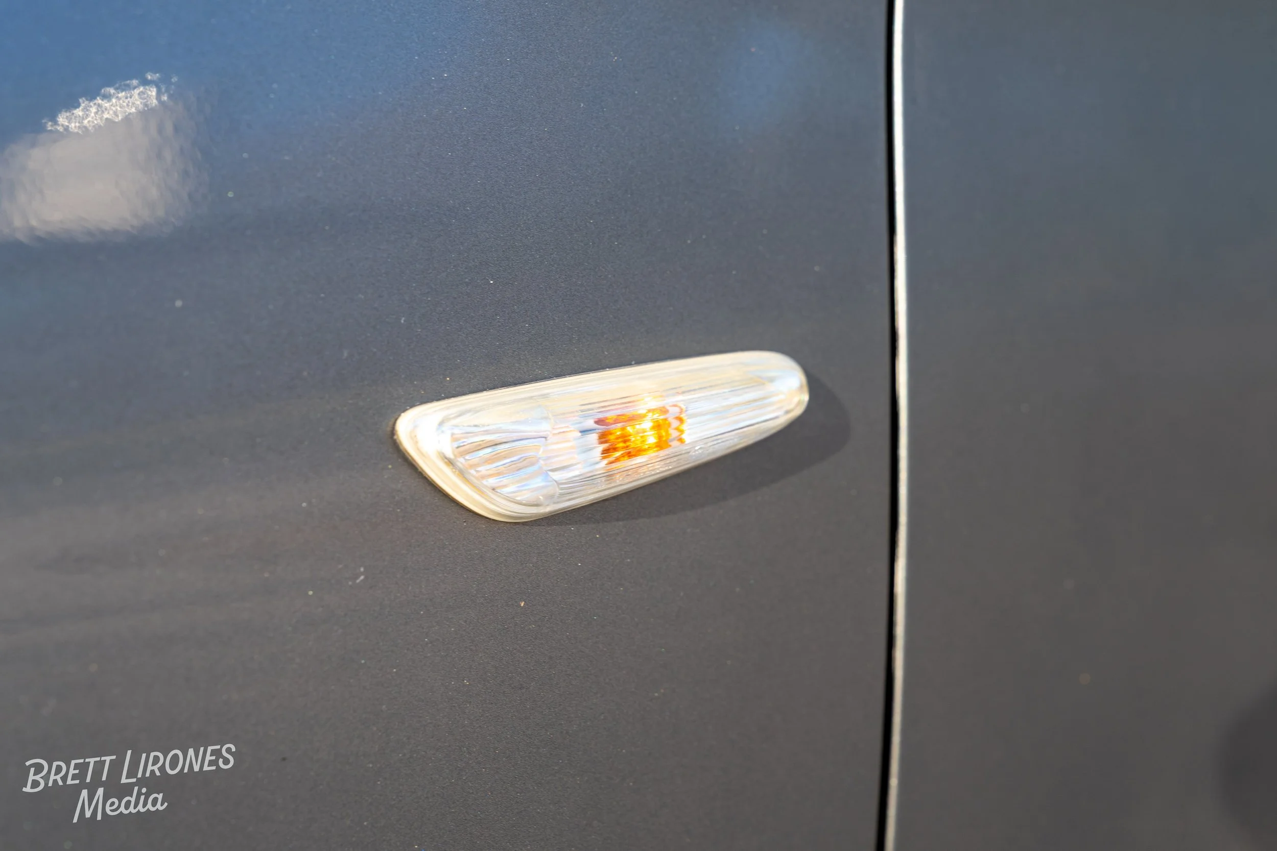 Close-up of a car's side marker light with the reflected sky in the background.