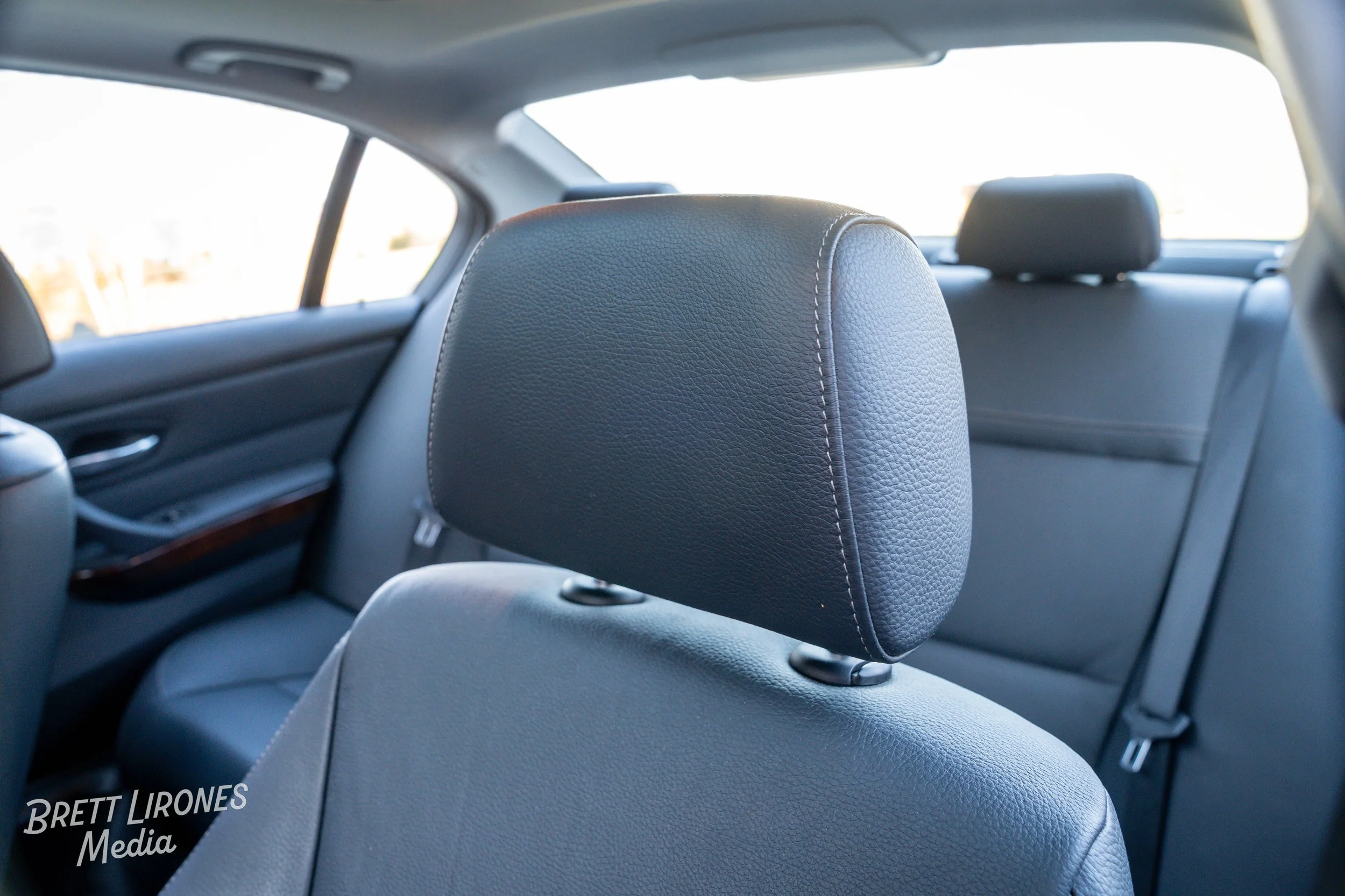 Interior of a car showing the back of the driver's seat with a headrest, and the rear seats with headrests, in a well-lit setting.