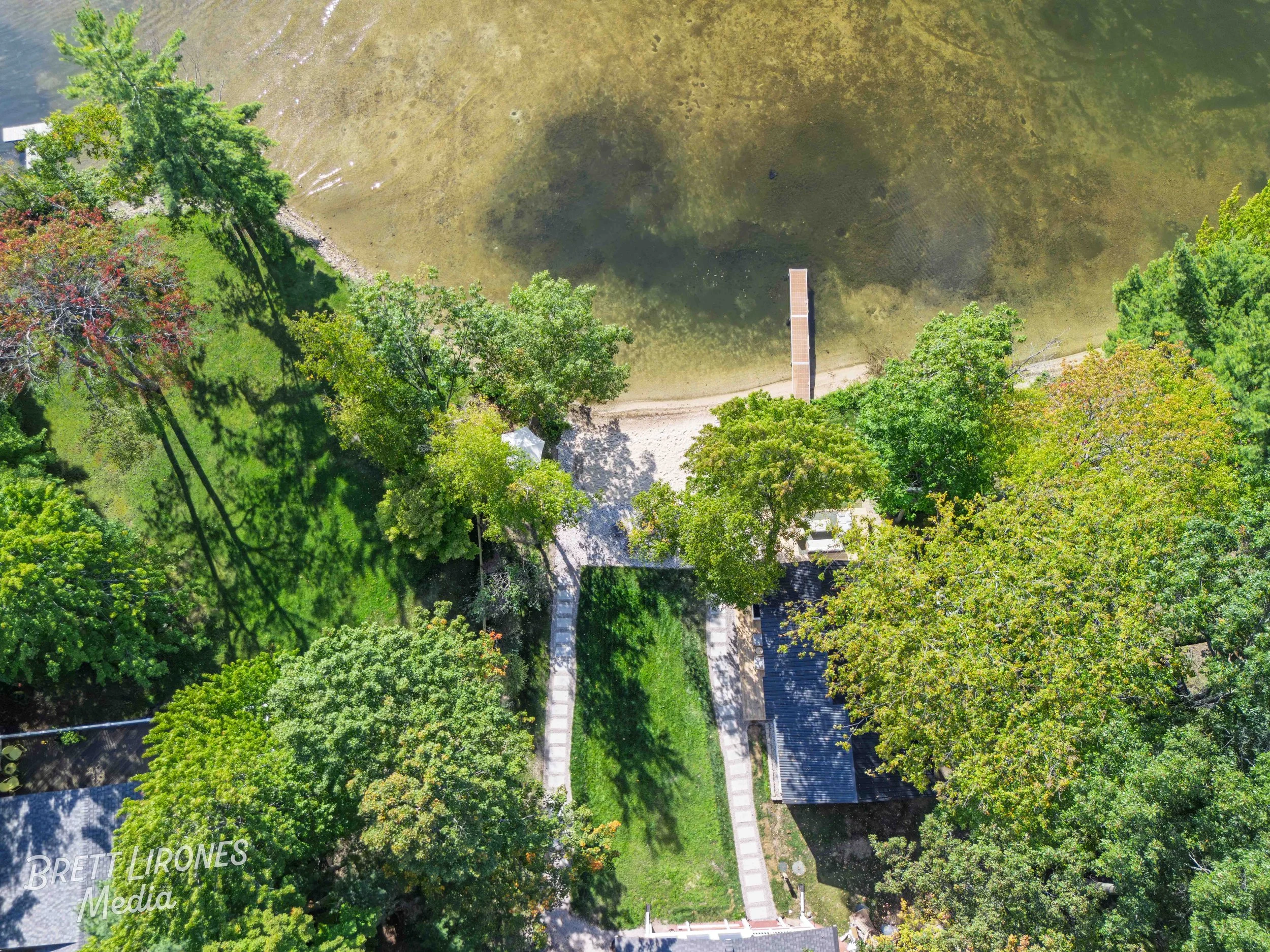 Aerial view of a park with green trees, a sandy pathway, and a small pond or lake with a dock.