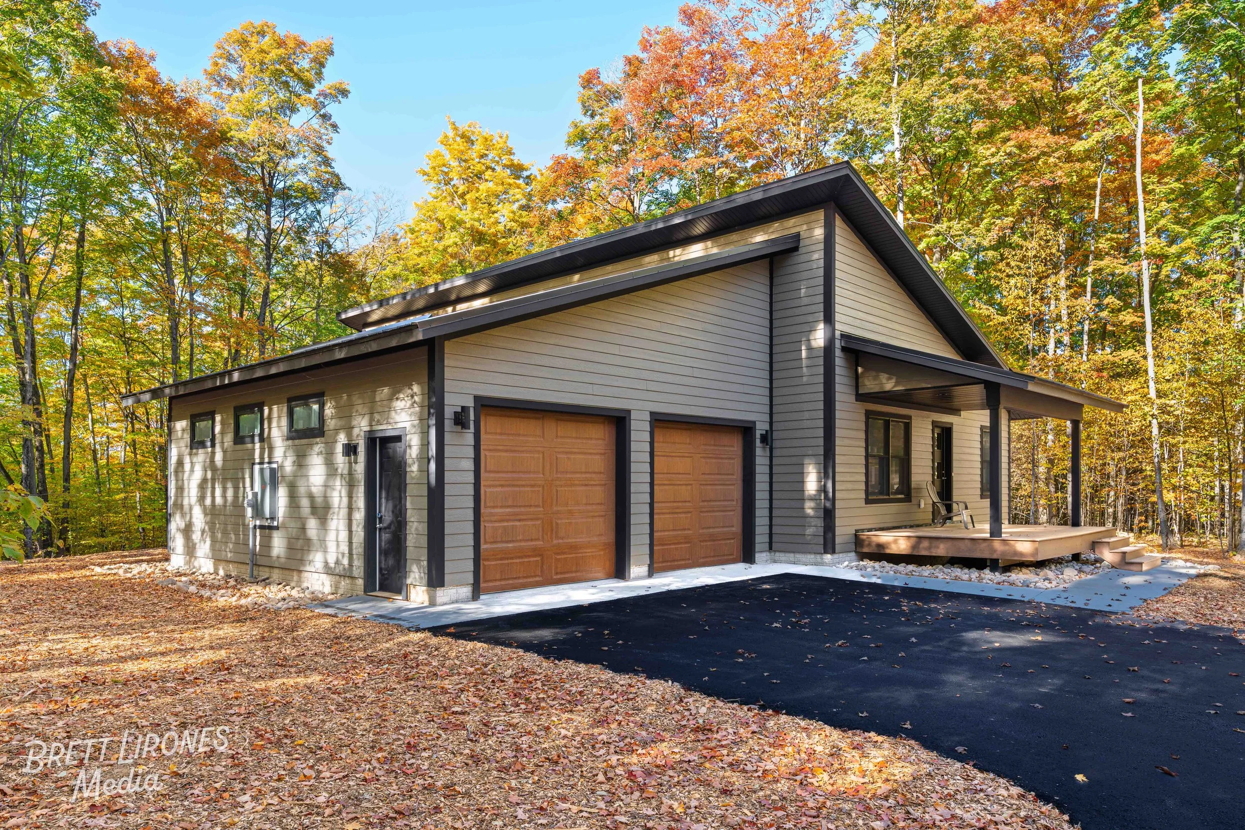 Modern house with two garage doors, small porch with two chairs, surrounded by fall foliage.