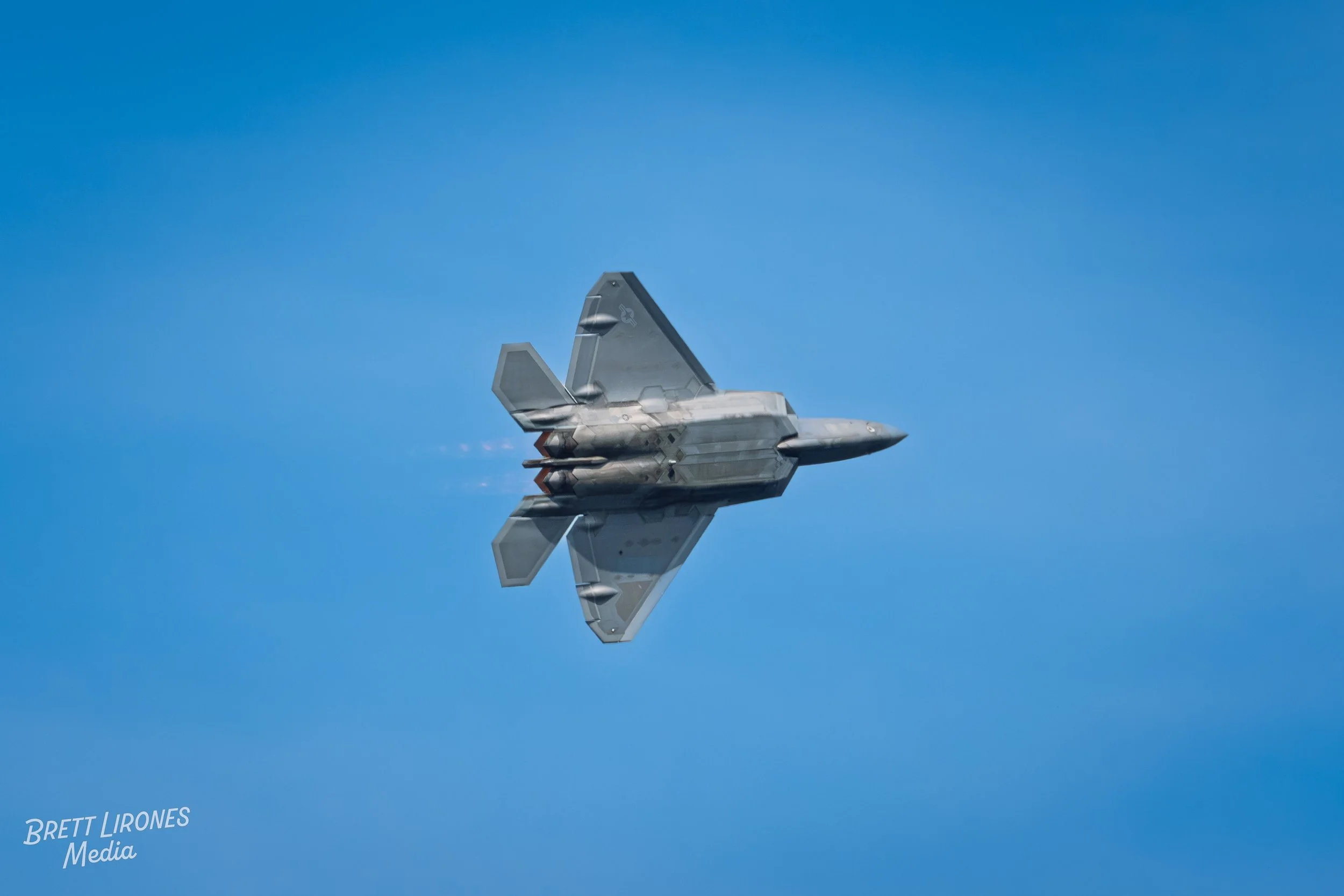 A fighter jet flying in clear blue sky, leaving a trail of vapor behind.