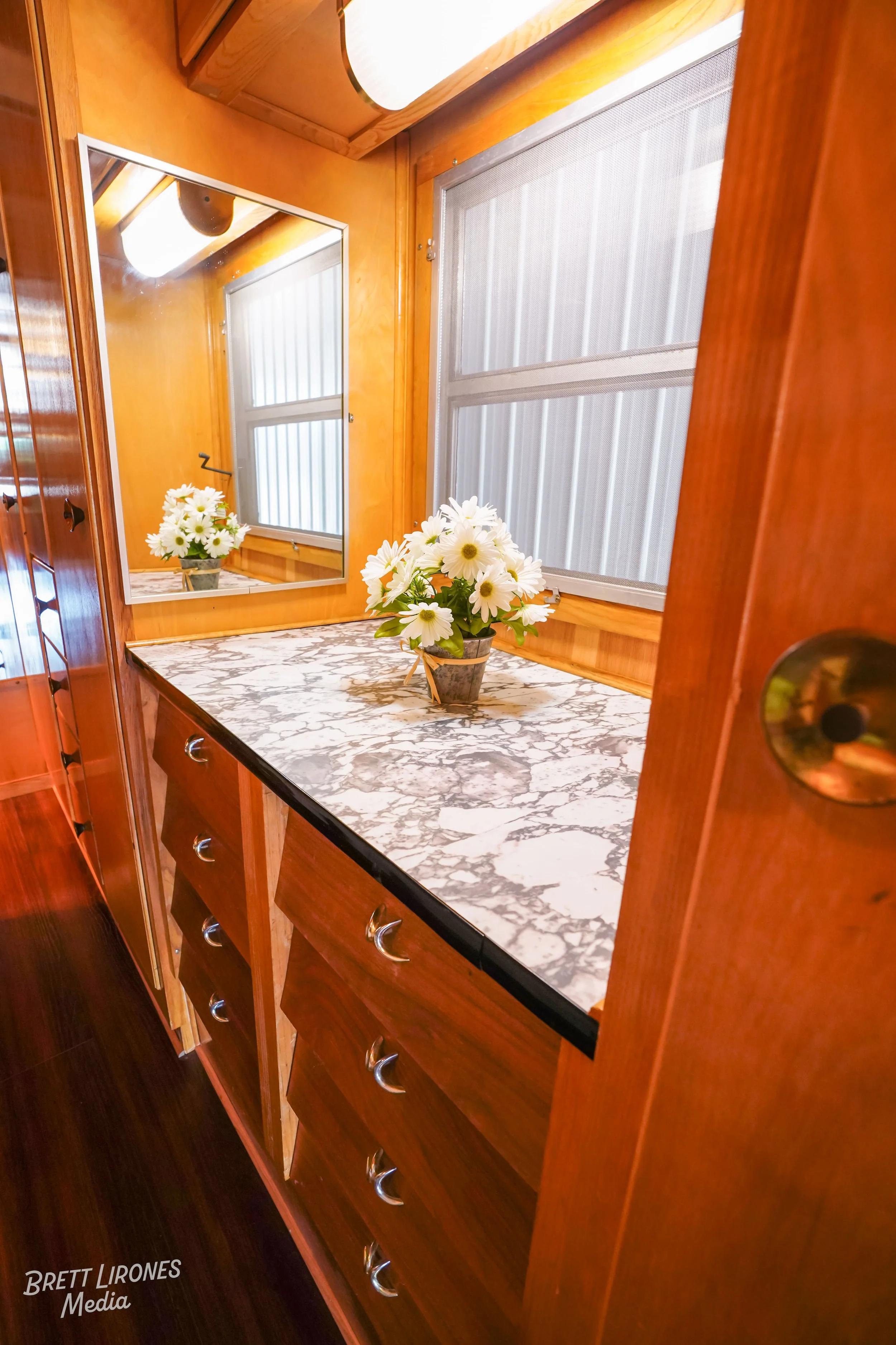 A small marble countertop with a flower vase, next to a window with blinds, within a wooden interior.