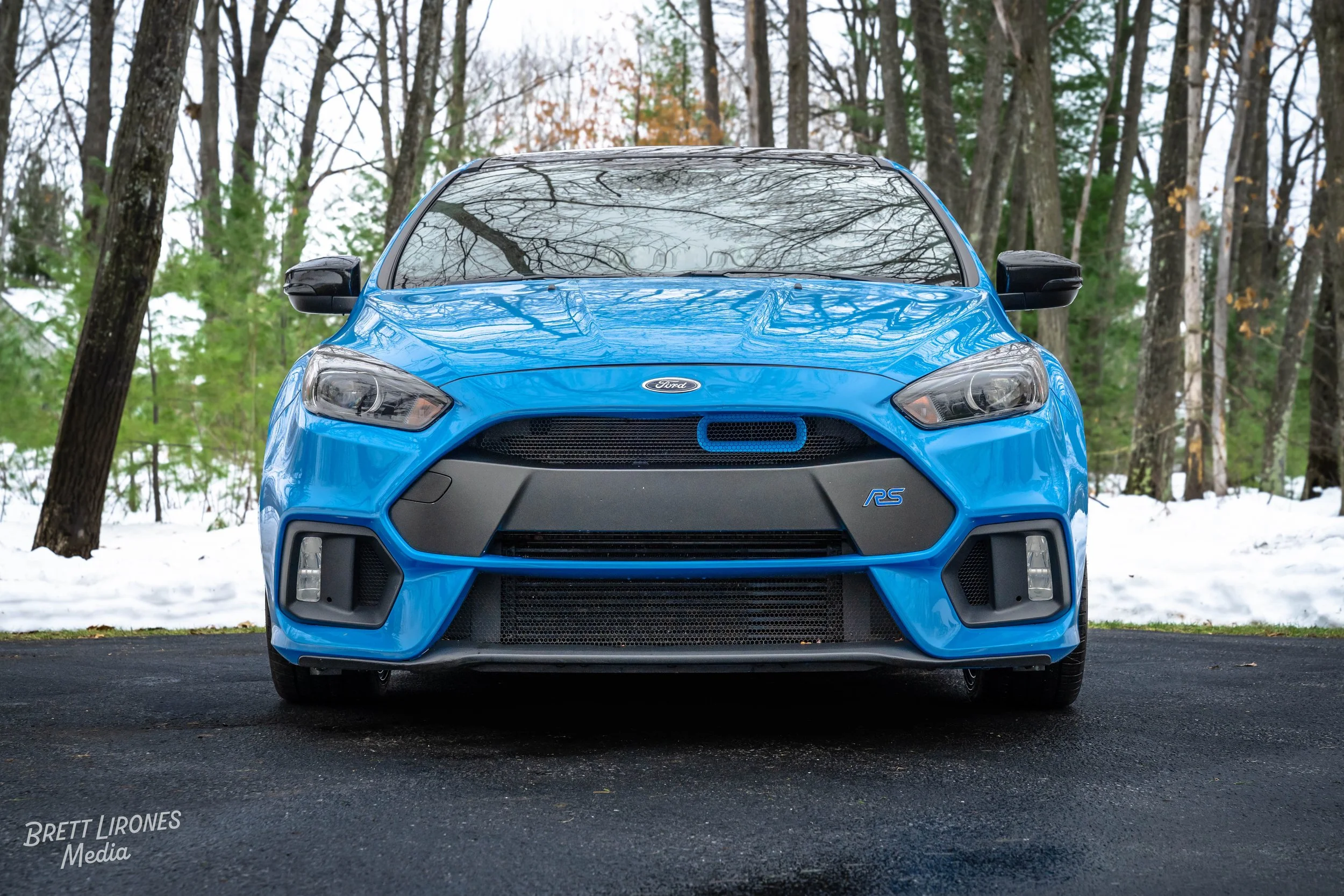 Front view of a blue Ford Focus RS parked on a driveway with snow and trees in the background.