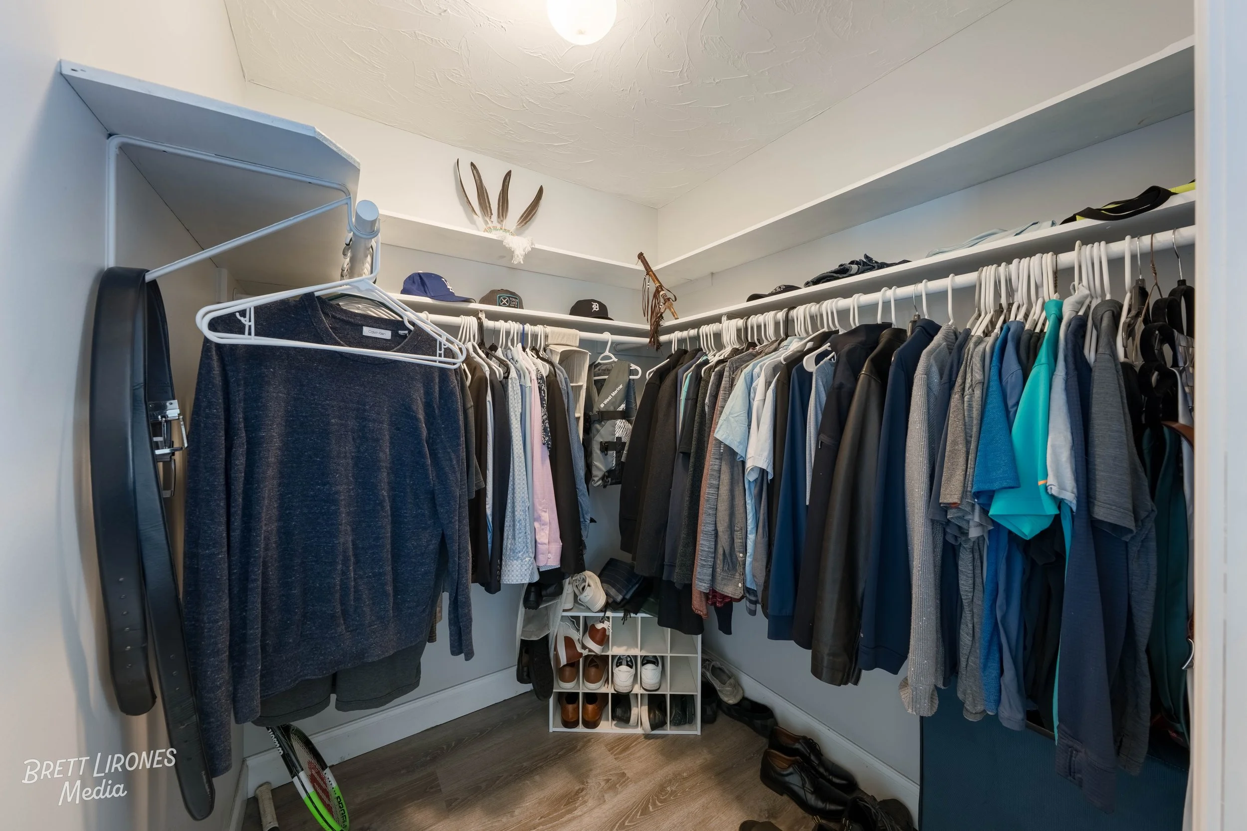 Clothes hanging on a white rod in a walk-in closet, with shoes on a cubby shelf below, and various accessories on the top shelf