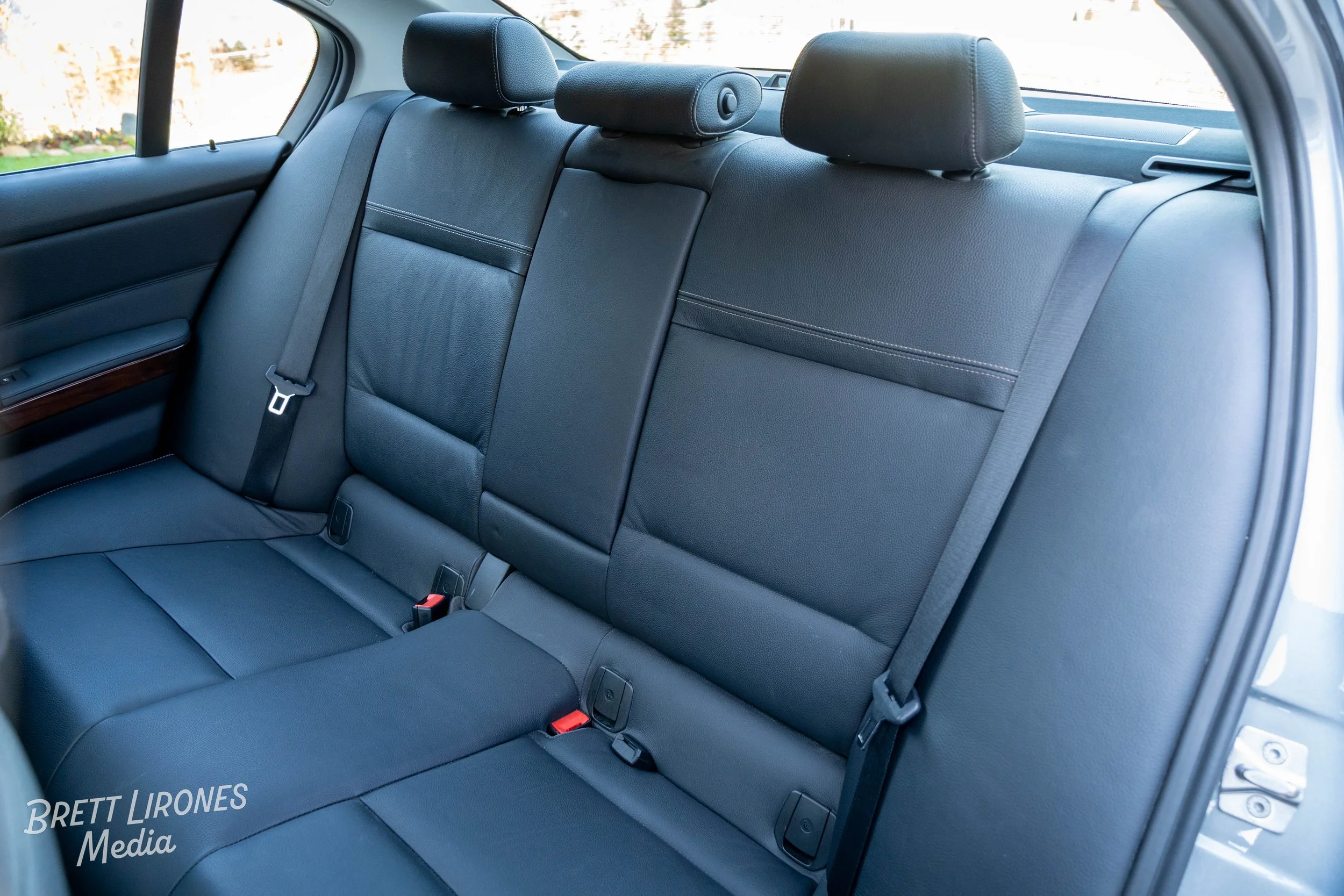 The back seat of a car with three headrests, three seat belts, and black leather upholstery.