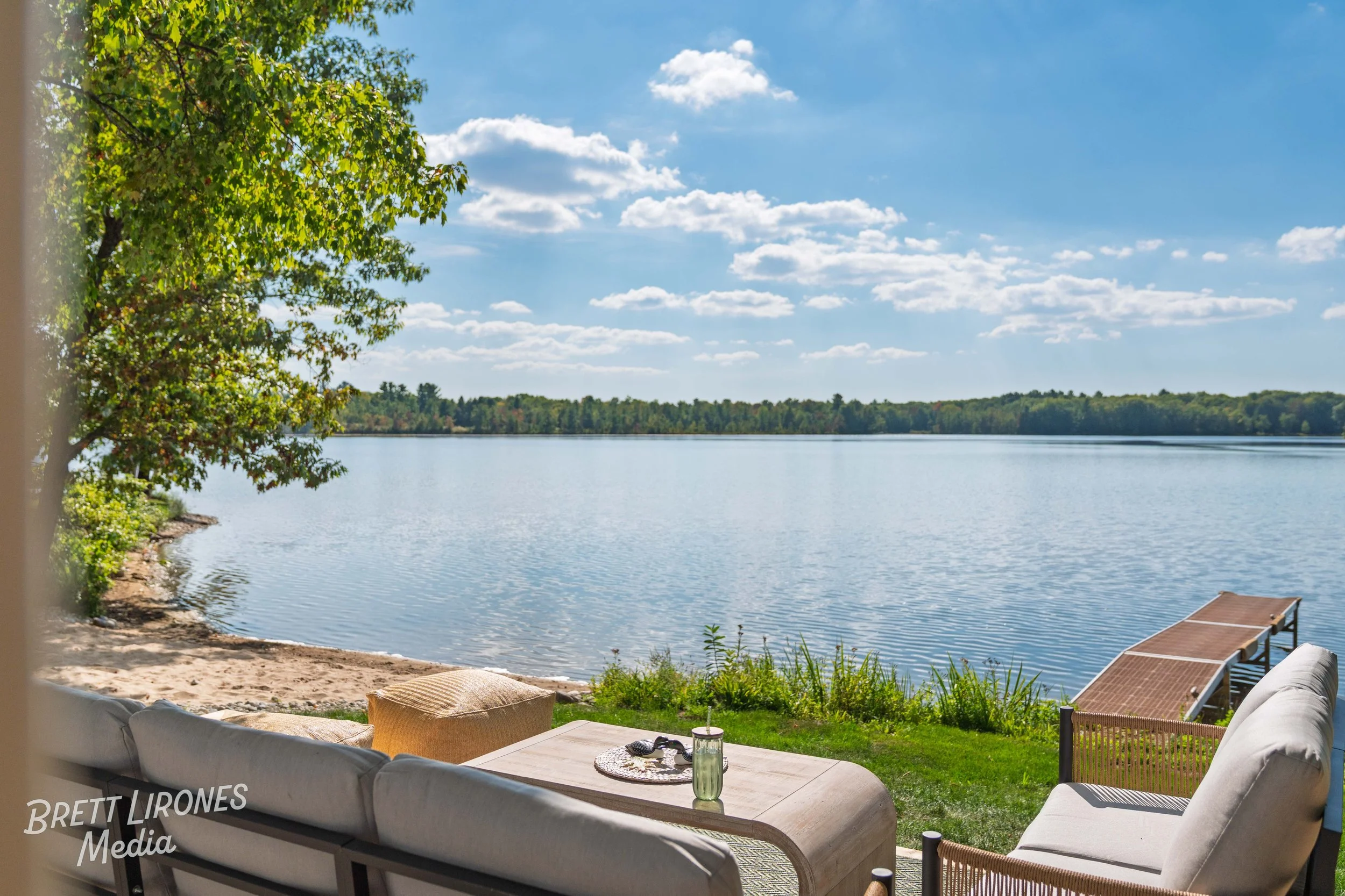 Outdoor patio with seating overlooking a lake under a blue sky with scattered clouds