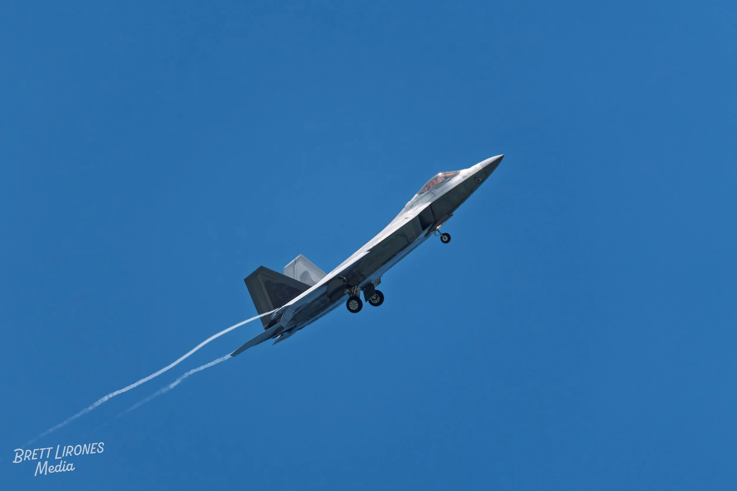A jet airplane flying in a clear blue sky with contrail behind it.