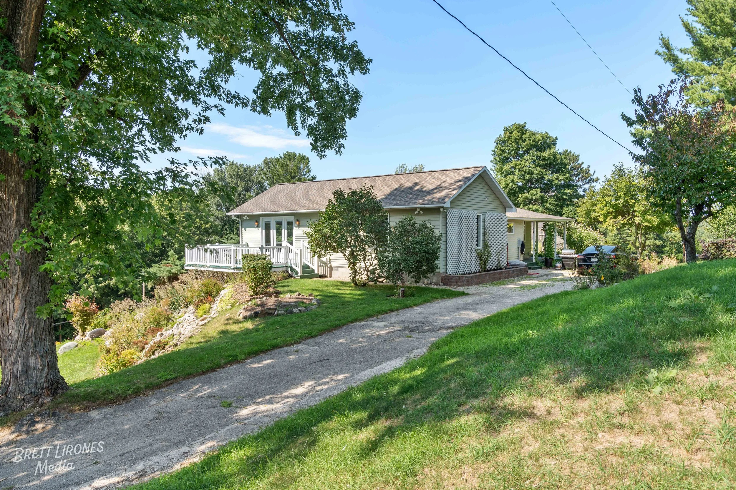 A house with a landscaped yard, a driveway, and trees, under a blue sky.