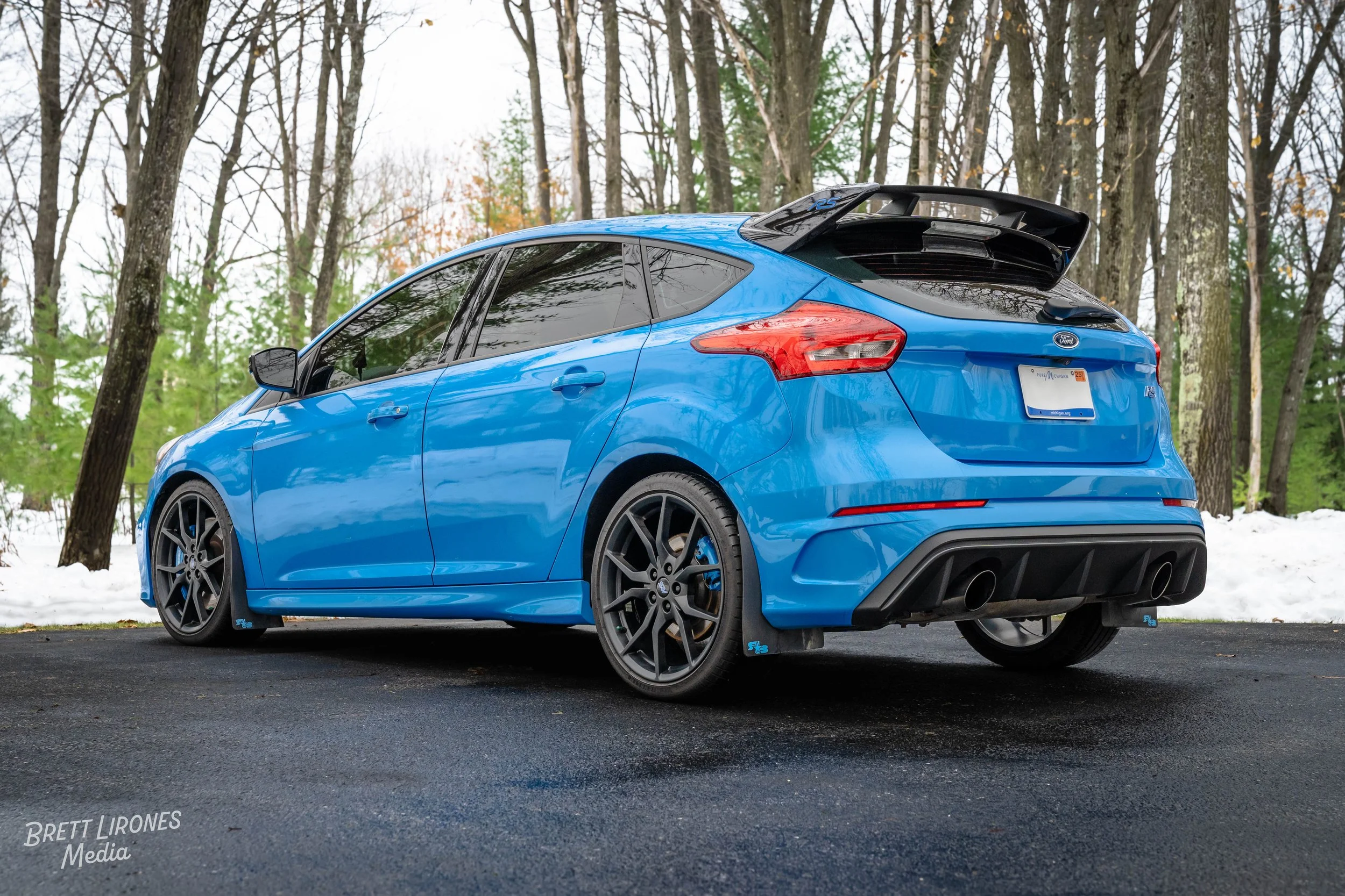 Blue Ford hatchback parked on asphalt driveway with snow and trees in the background.