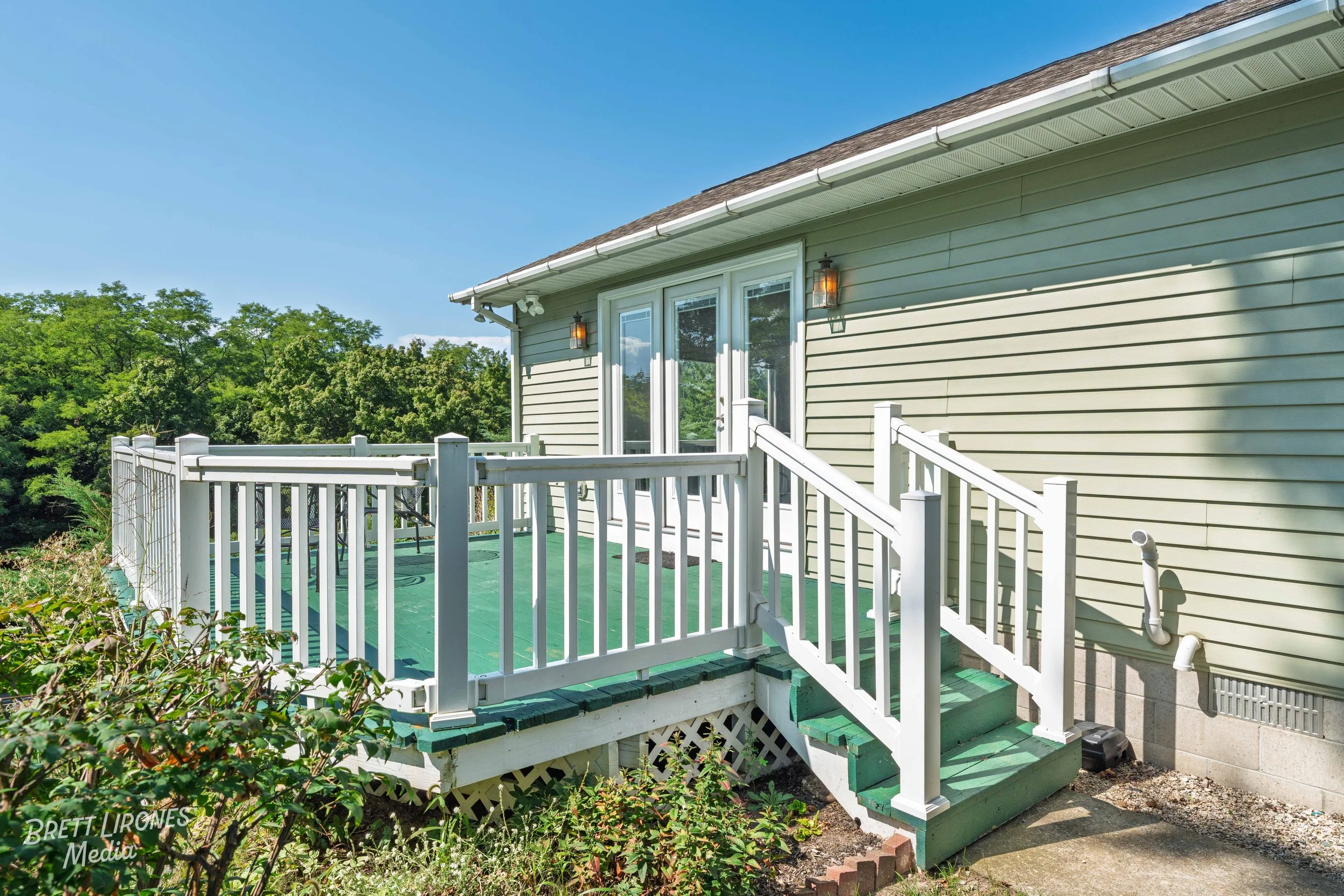 Backyard deck with white railing and green flooring outside a house with beige siding and sliding glass doors under a clear blue sky.