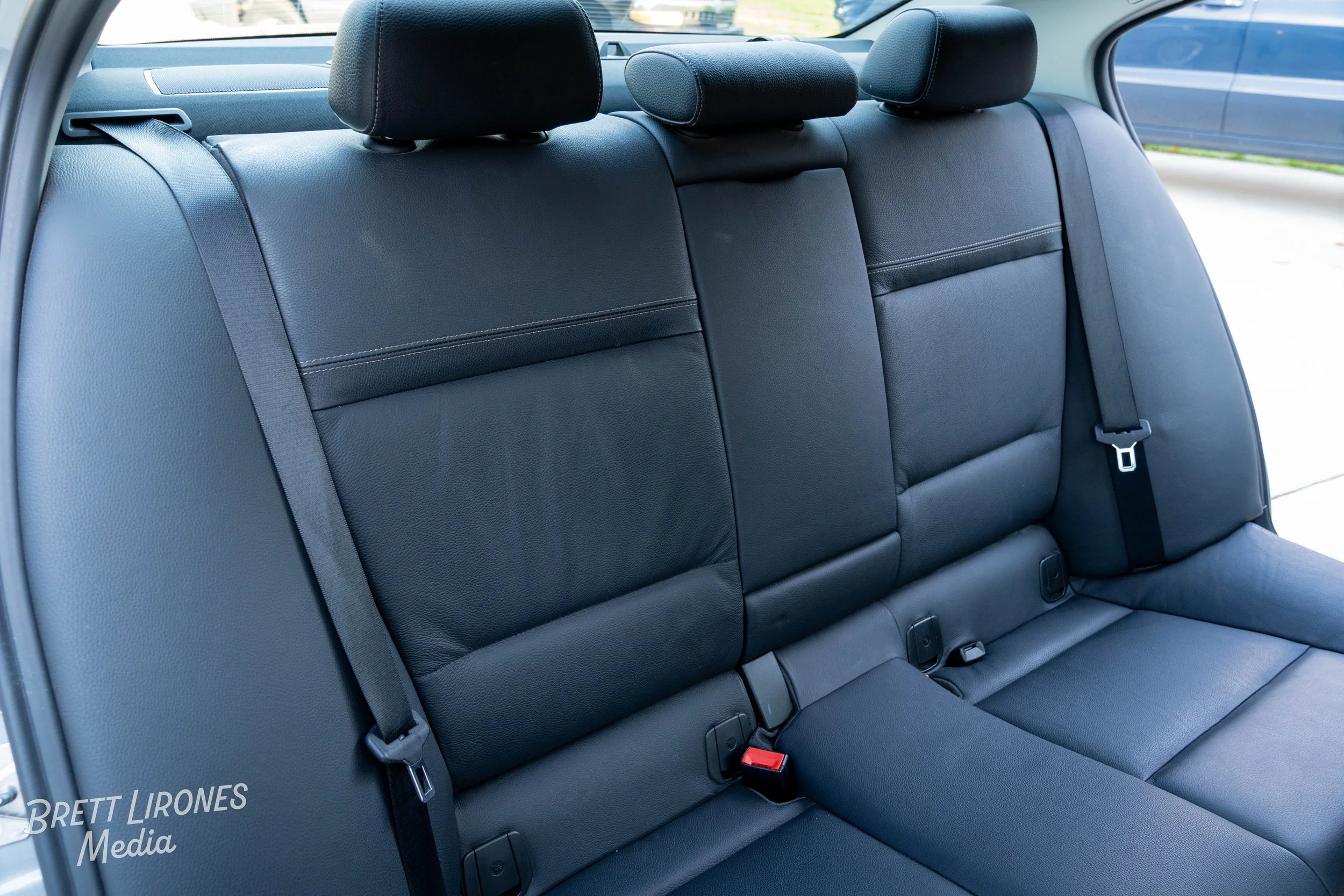 The backseat of a car with black leather seats and seat belts.