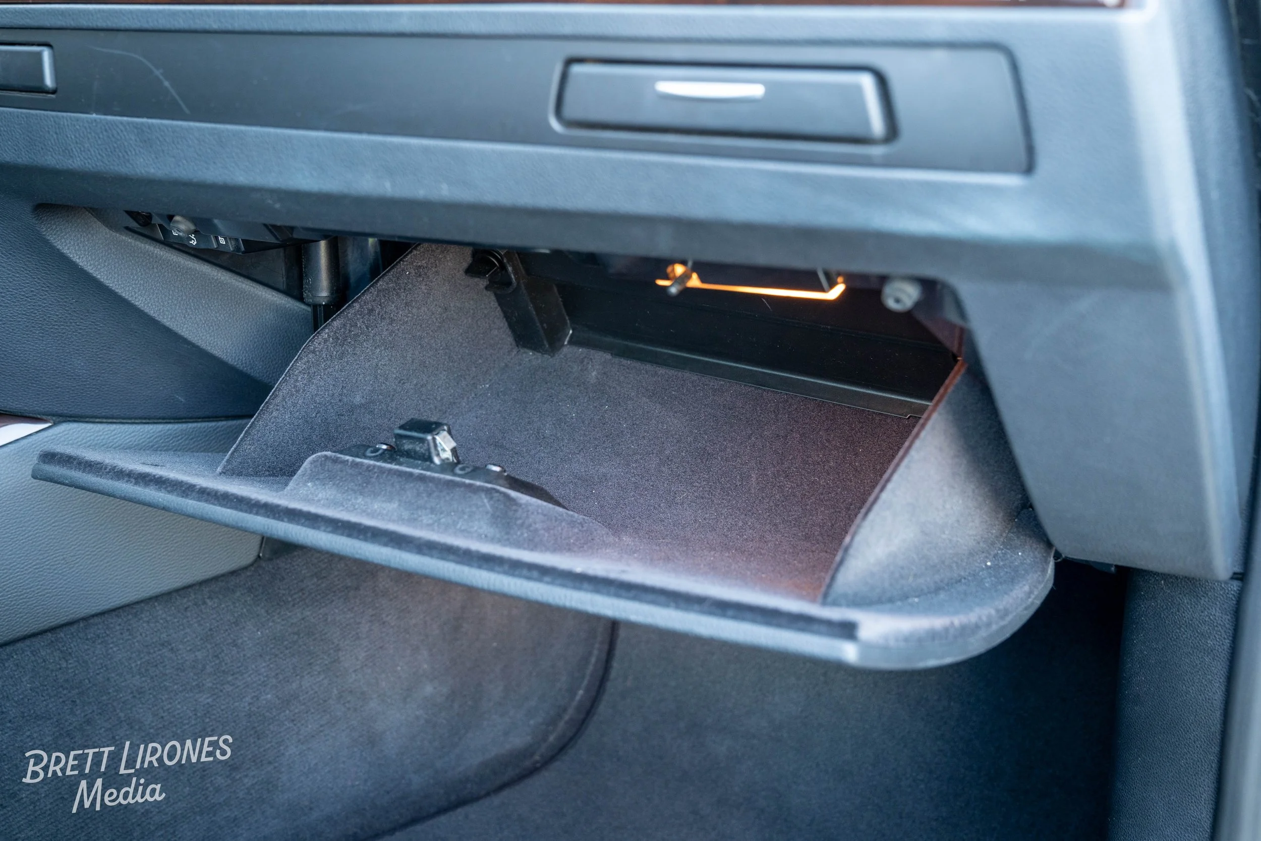 Open glove compartment in a car's dashboard, empty inside with interior lighting visible.